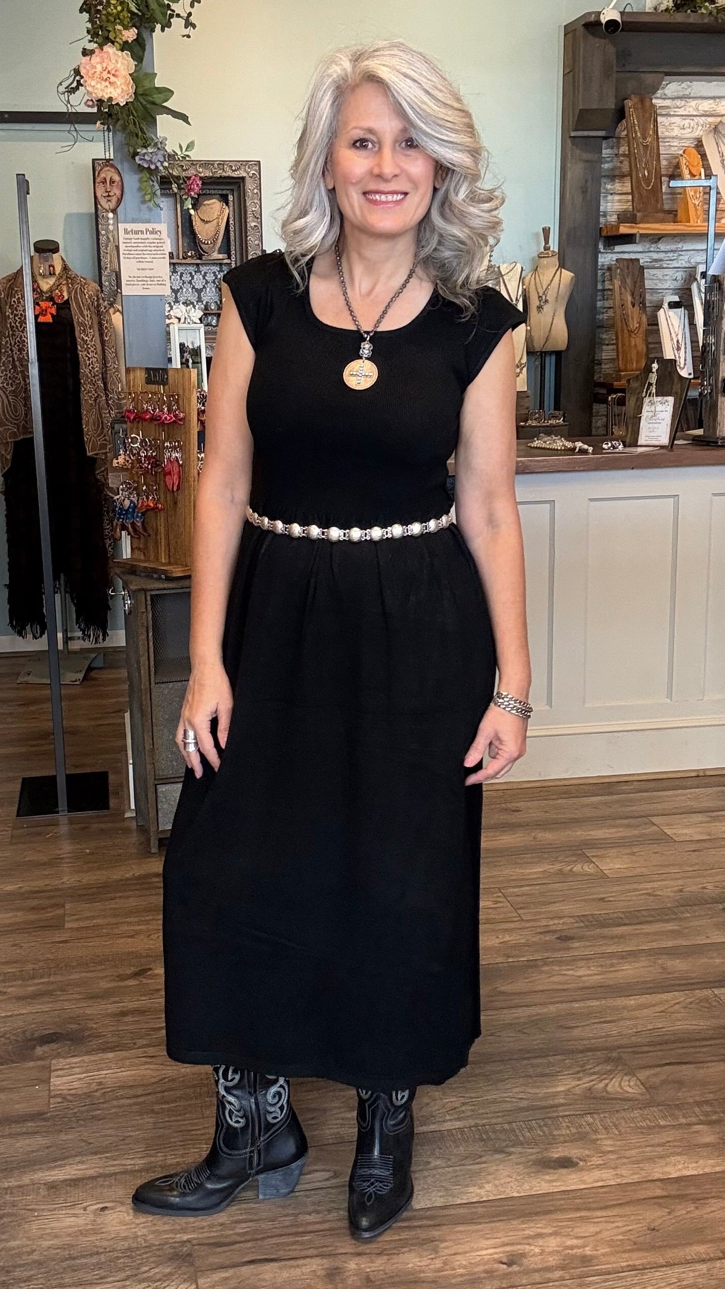 Woman in a black dress standing in a store with mannequins and clothing in the background.