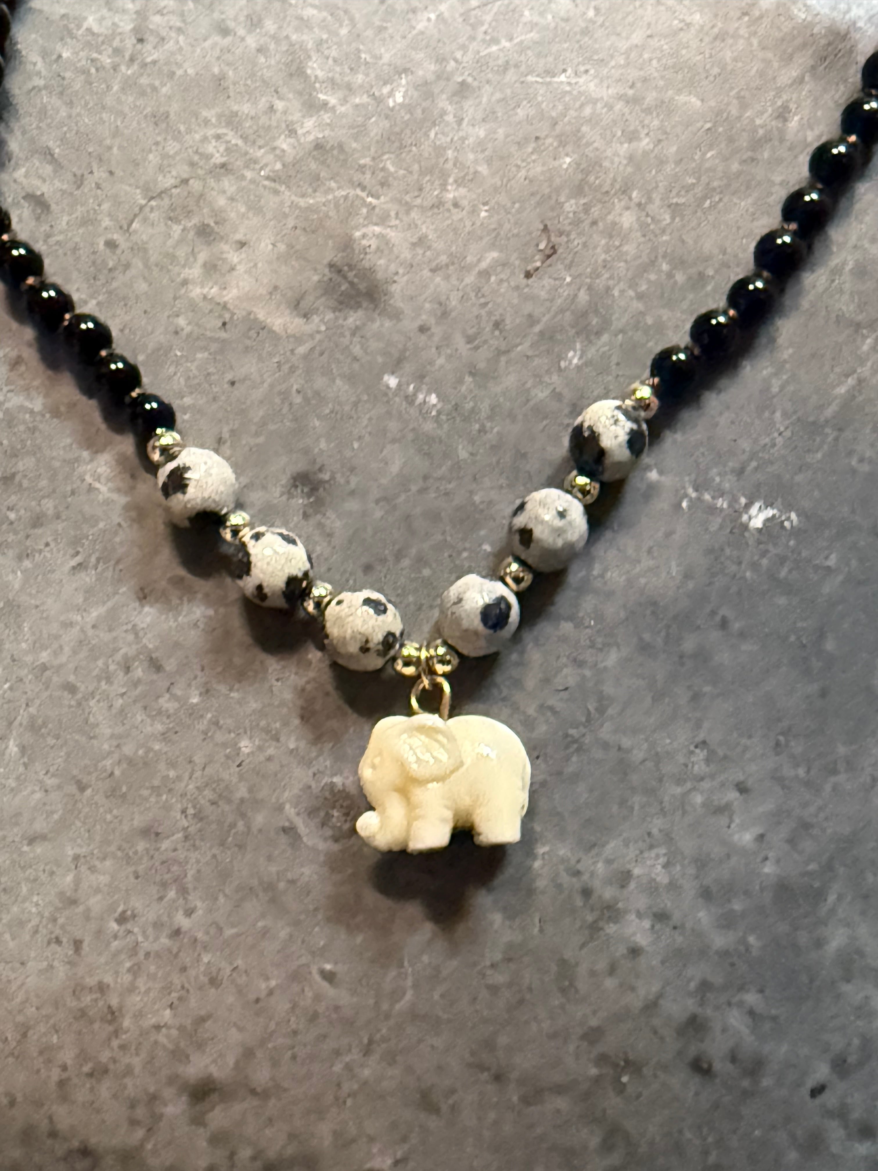 Necklace with black beads and a white elephant charm on a gray surface