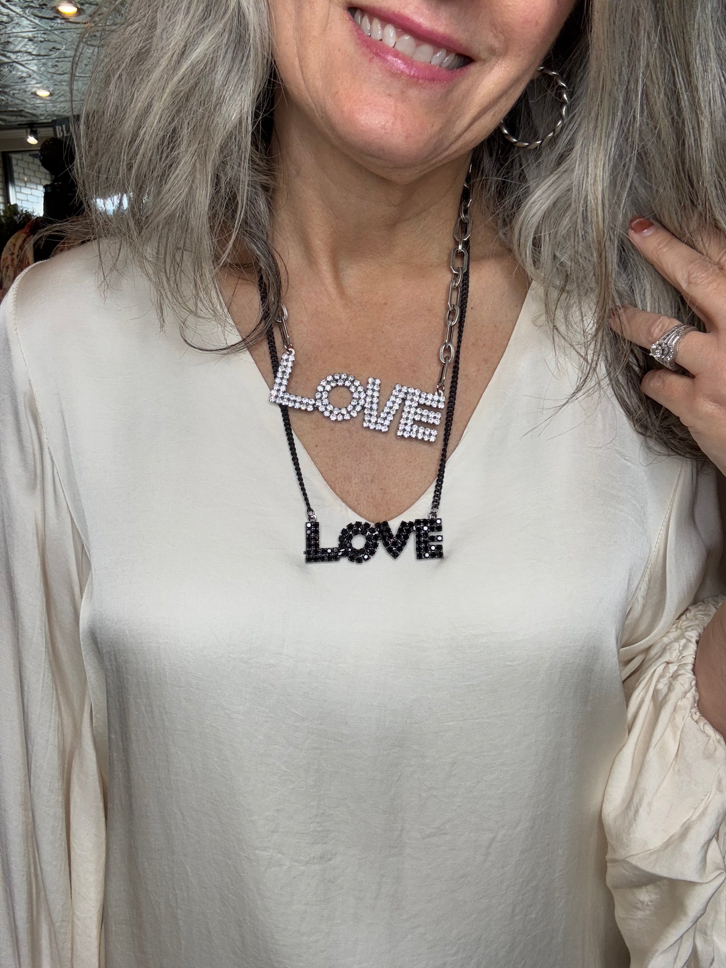 Person wearing two LOVE necklaces, one black and one silver
