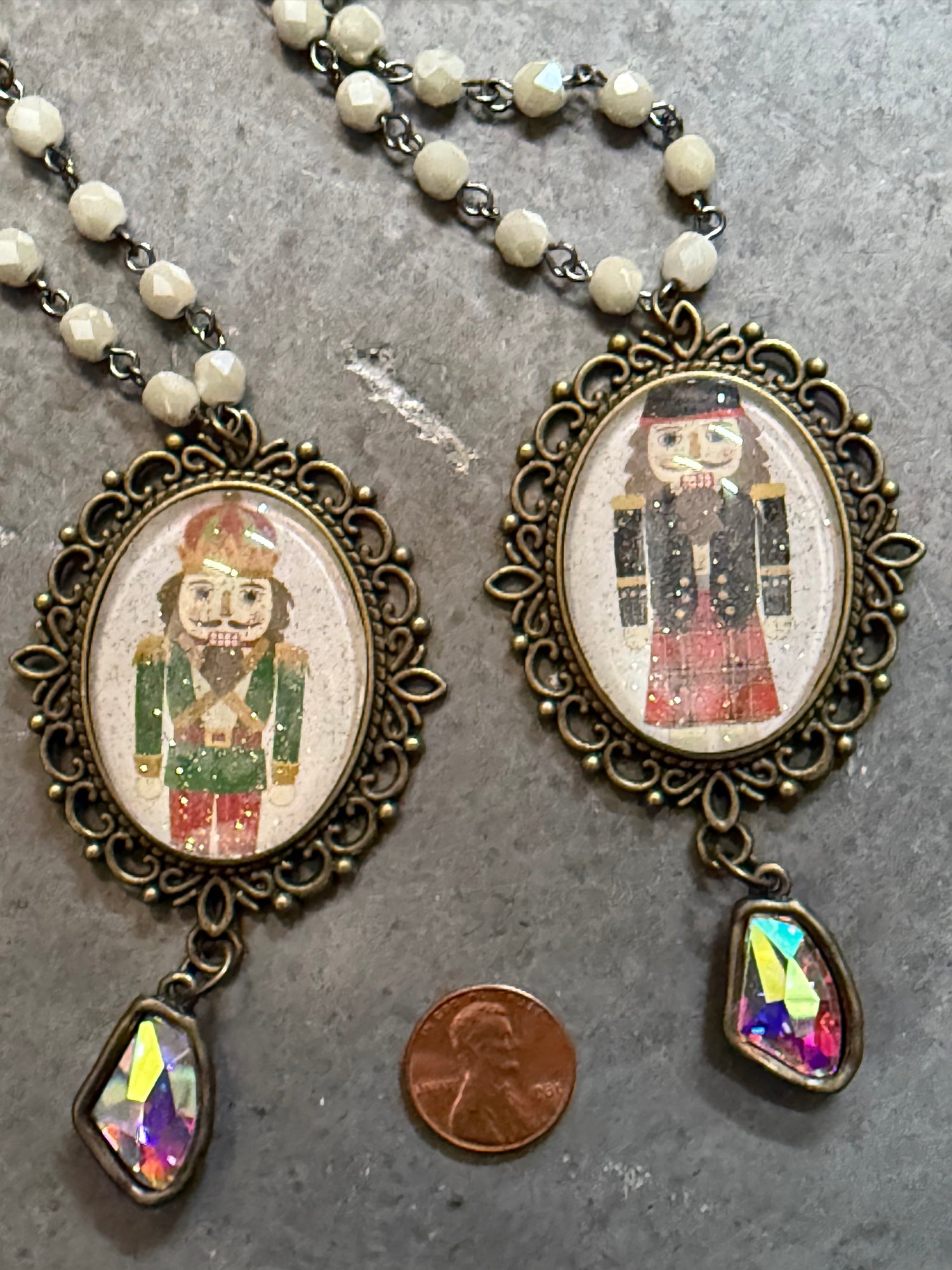 Two ornate necklaces with pendant images of a person in a suit on a gray surface.