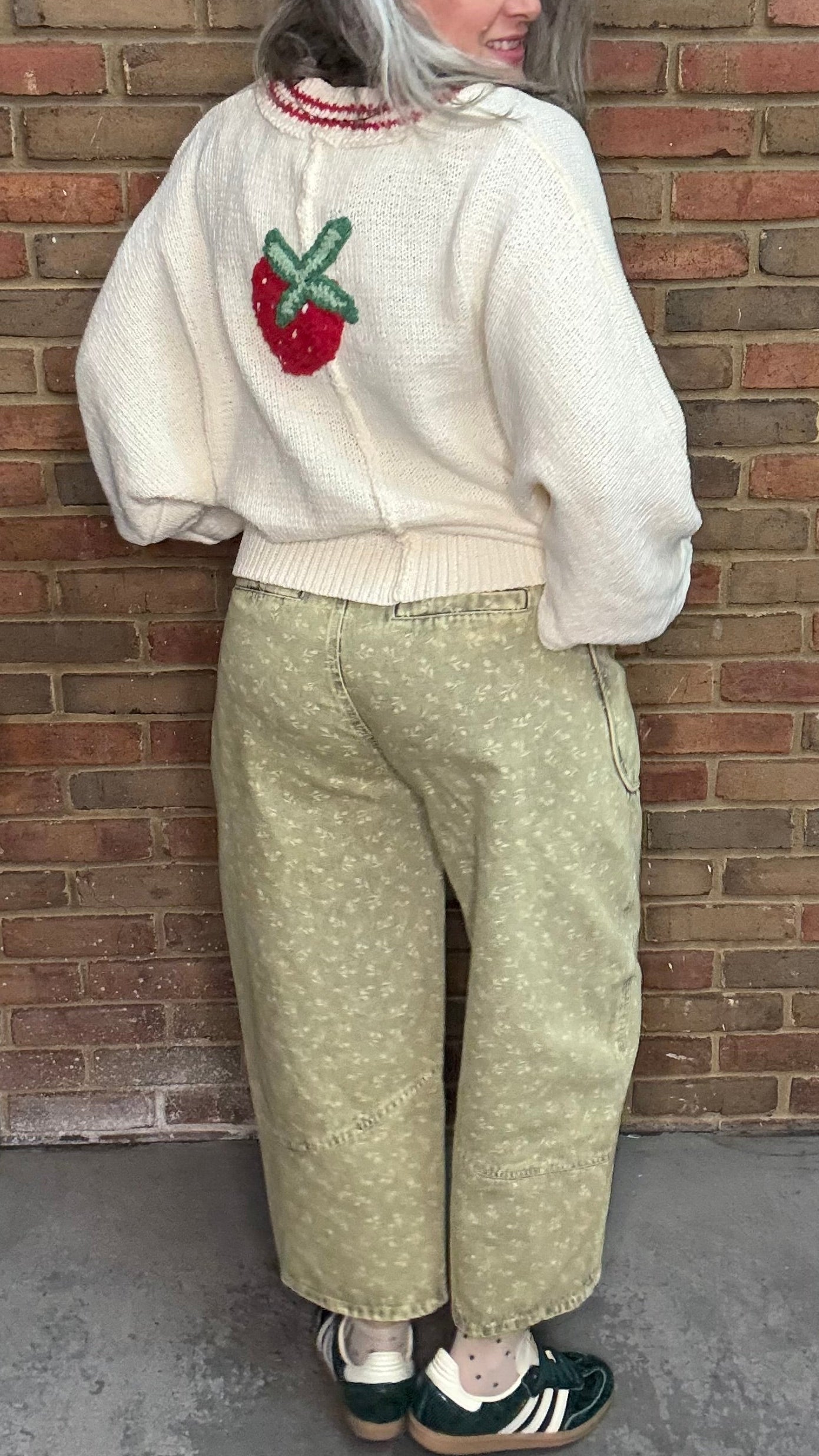 Person wearing the Strawberries on Cream Sweater and Floral Printed Barrel Pants standing against a brick wall.