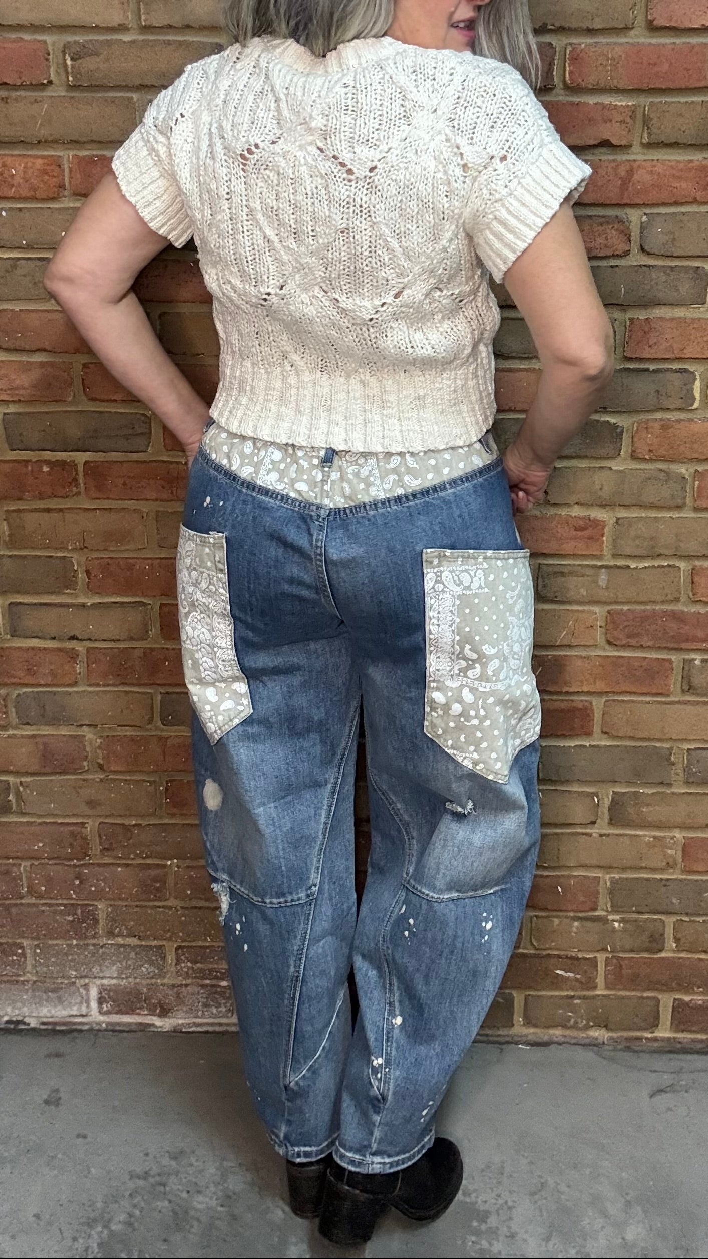 Woman standing in front of a brick wall wearing the Big Pocket Denim Pants and the Oatmeal Sweater Top.
