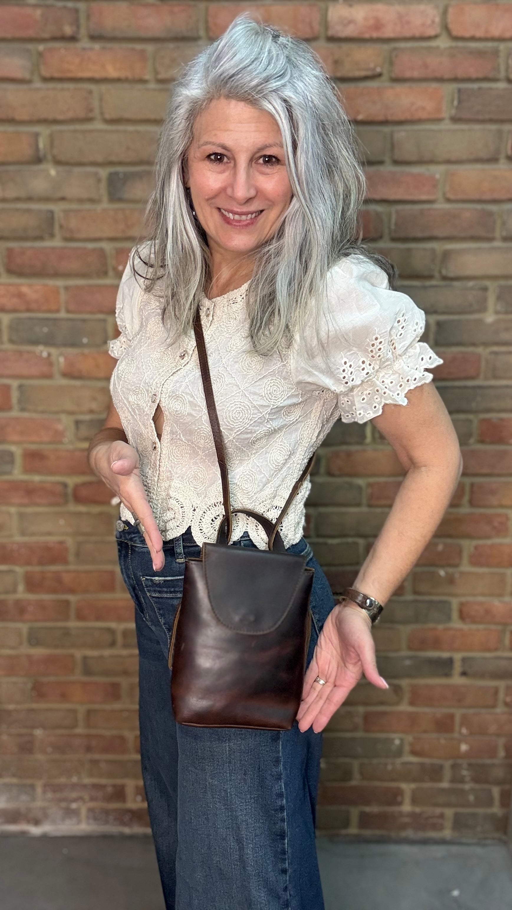 Woman holding a Backpack style leather Handbag with a brick wall in background.