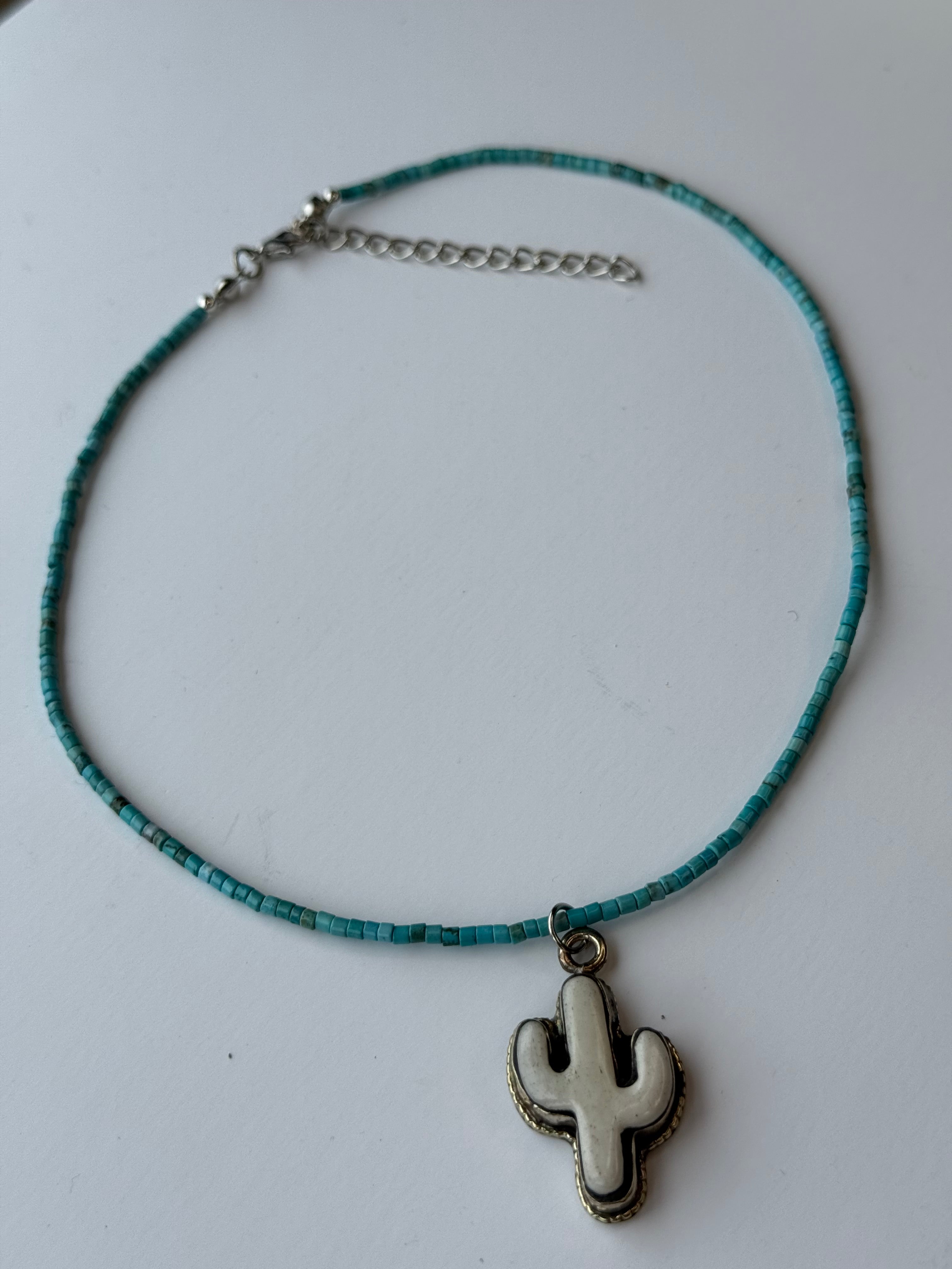 Necklace with turquoise beads and a white cactus pendant on a light gray background