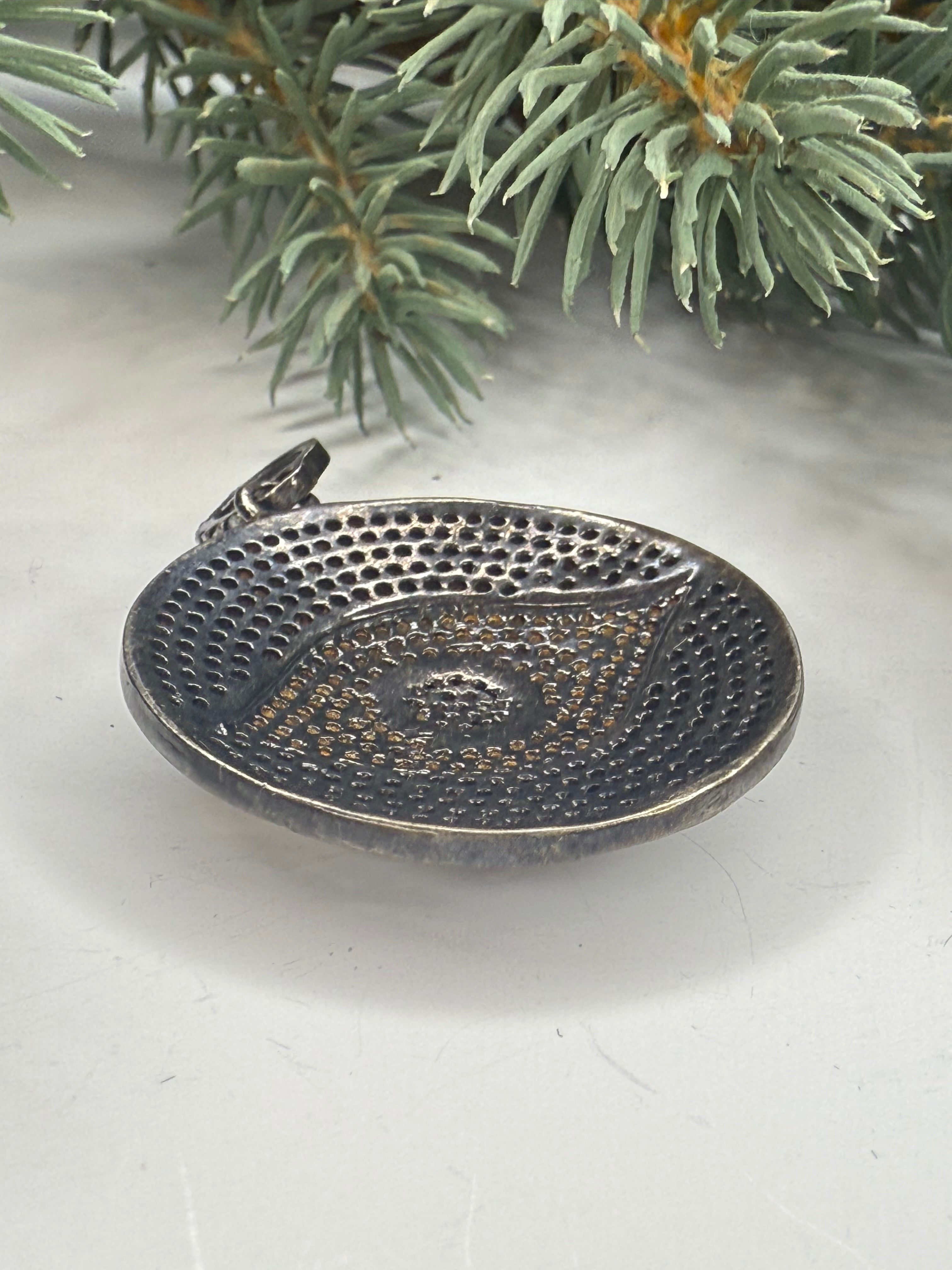 Metal pendant with textured surface on a white background with greenery