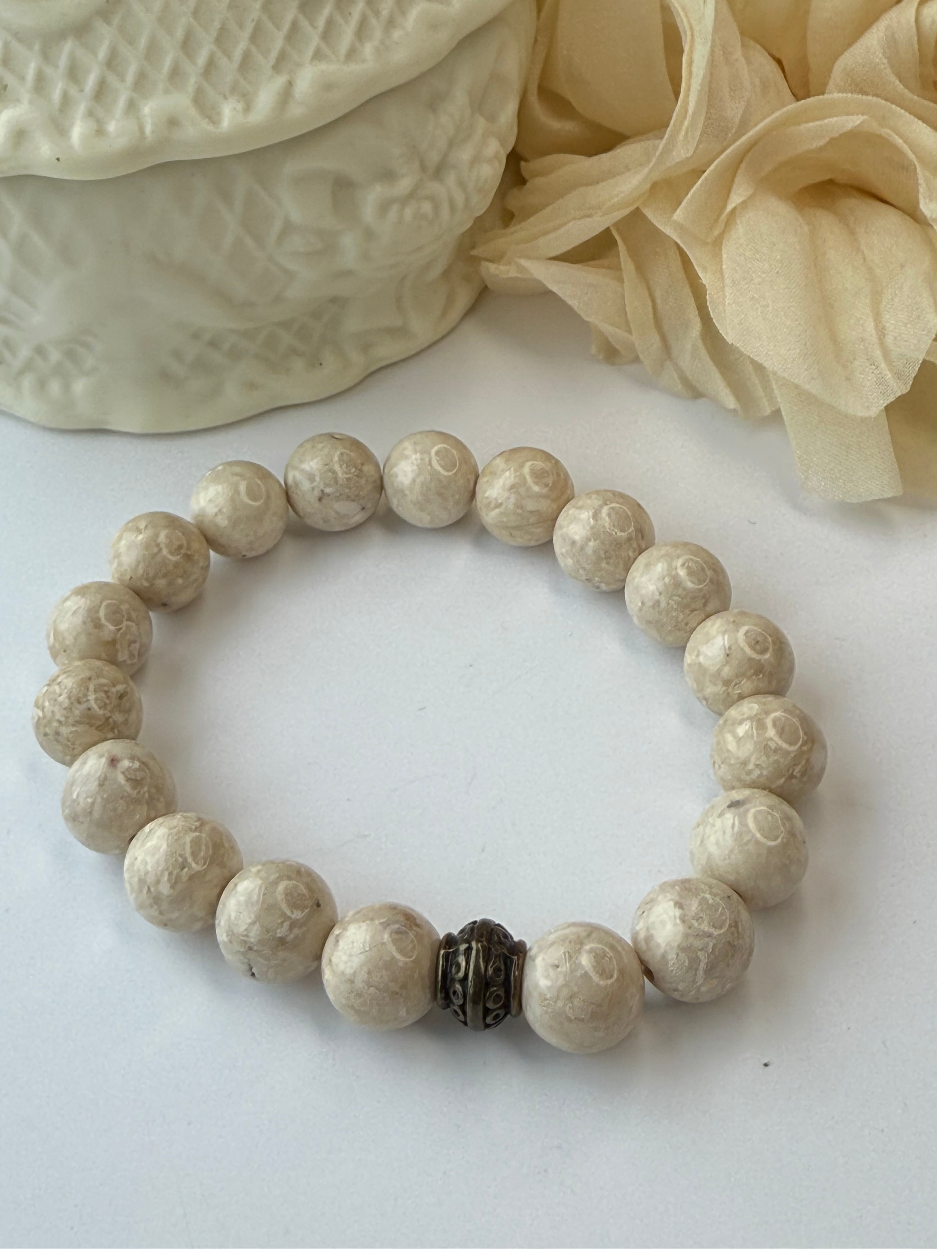 Beige beaded bracelet on a textured white surface with beige fabric and lace in the background