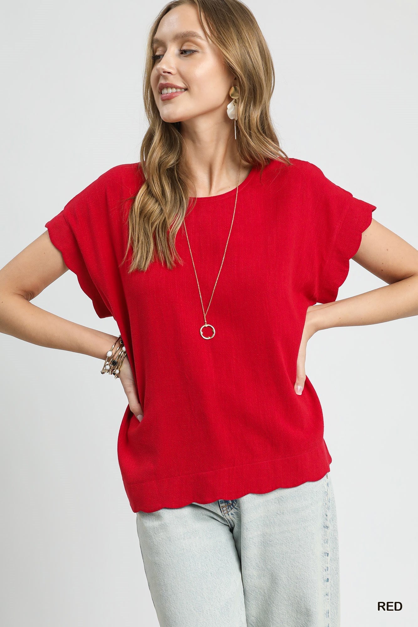 Woman wearing a red top and light jeans on a plain background