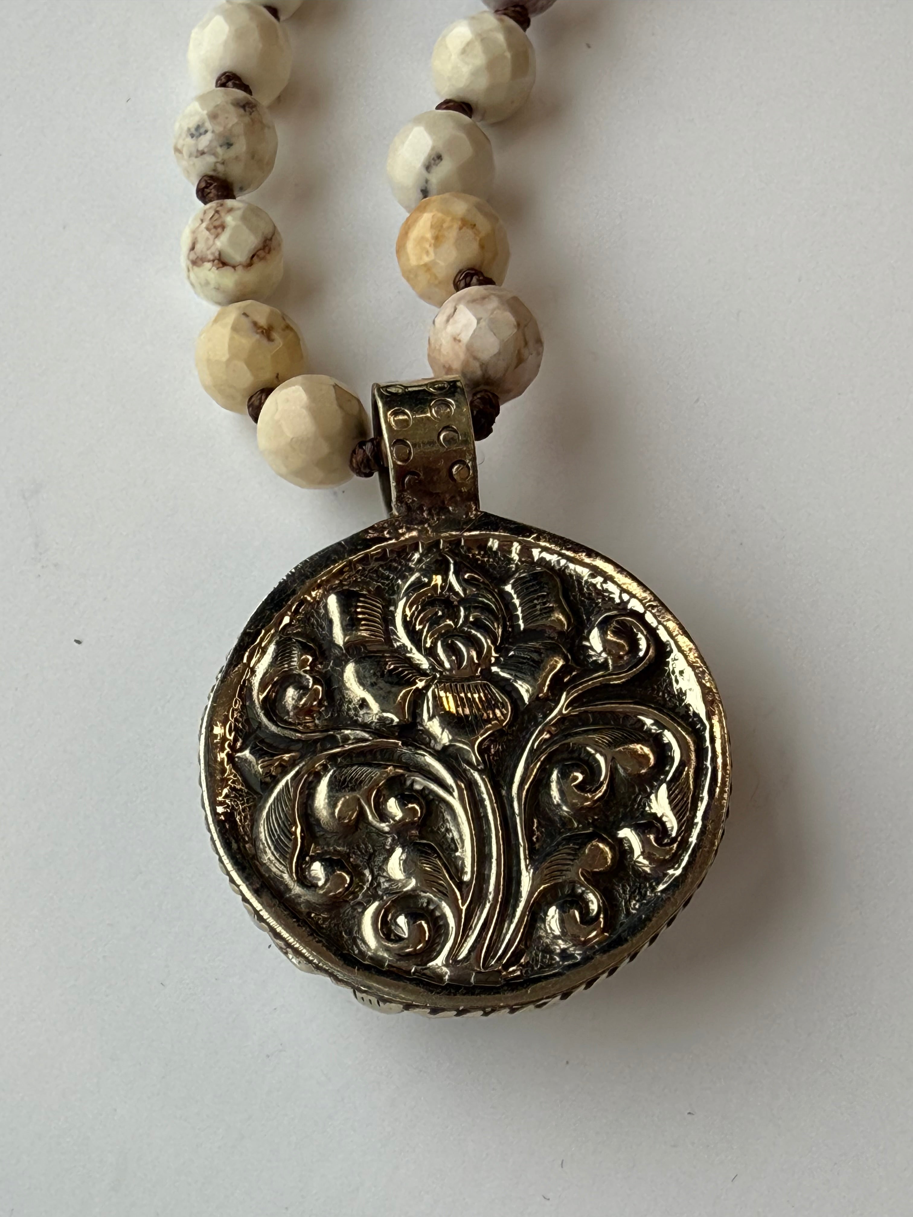 back of rose pendant on a beaded necklace with a white background