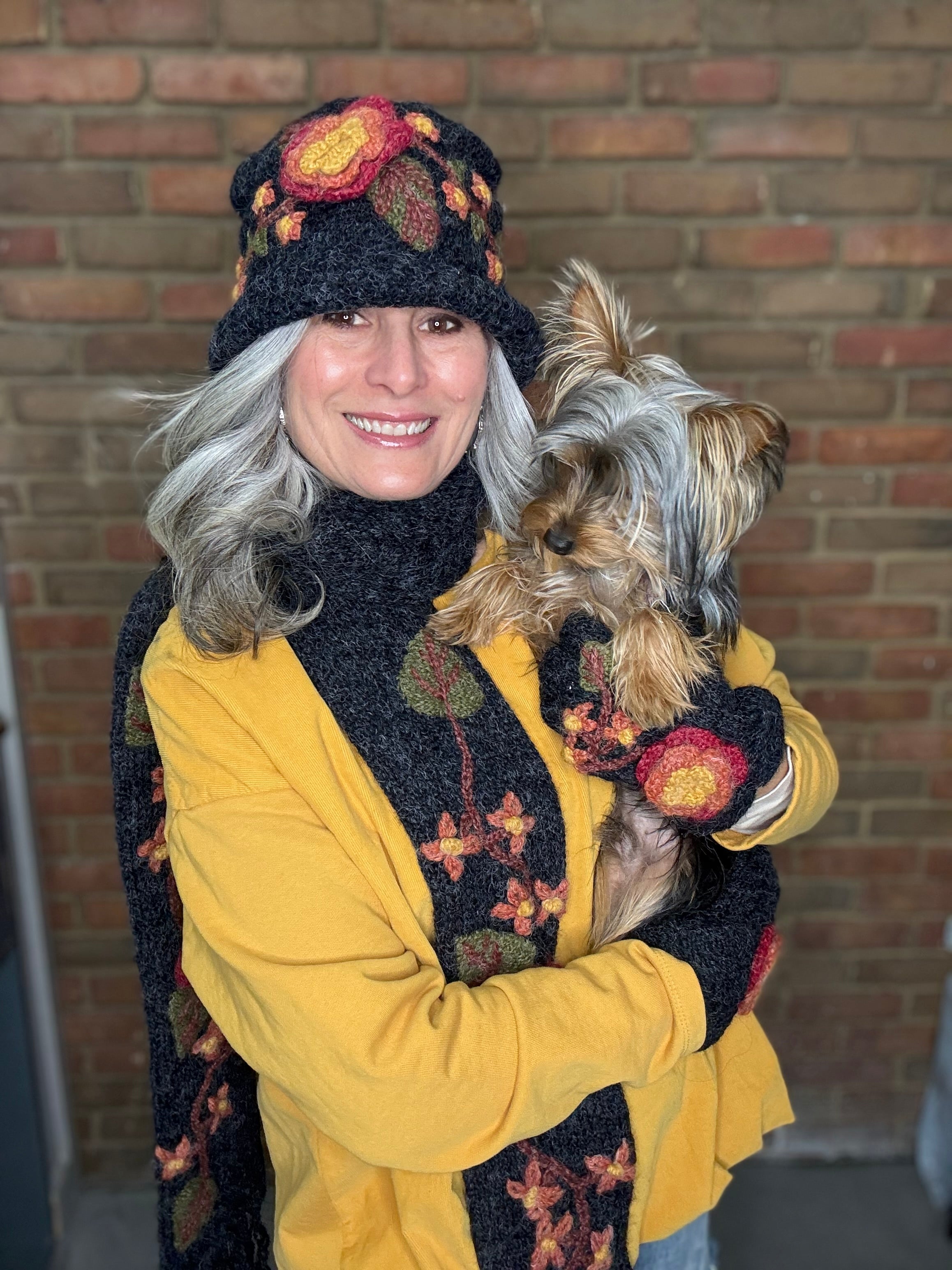 Woman wearing the Solid Mustard Puckered Pullover with a matching set of the Bouquet Hand Crochet Scarf, Hand Warmers, and Bucket Hat holding a Yorkie Dog.