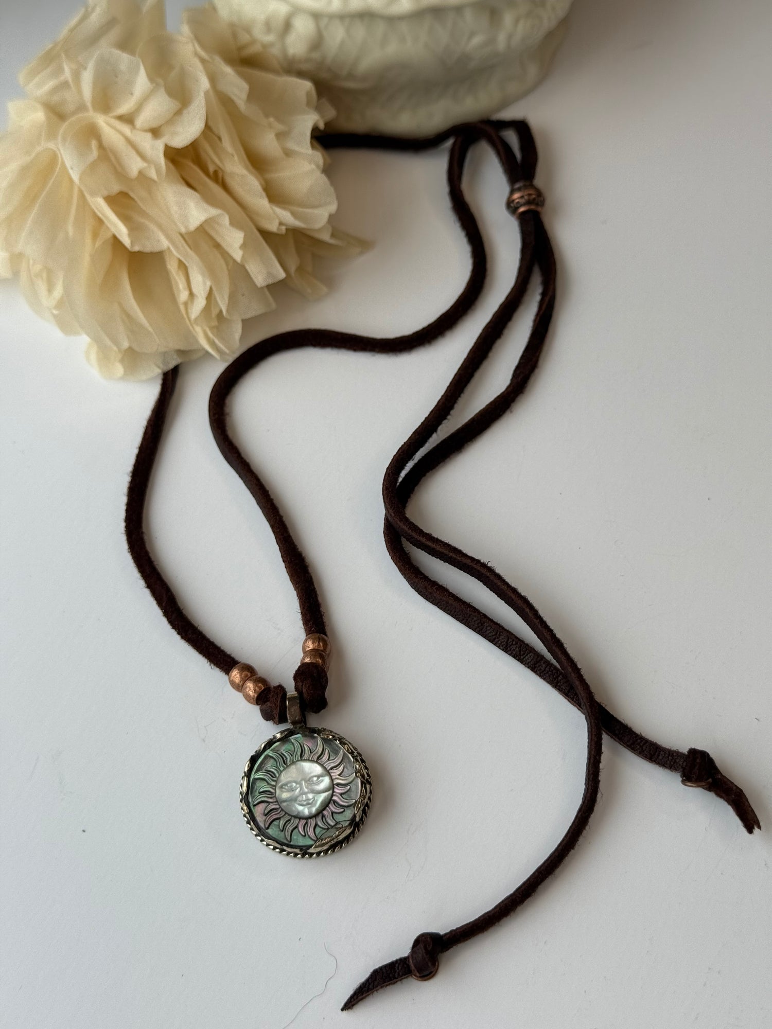 Necklace with decorative pendant on a white surface next to a beige flower