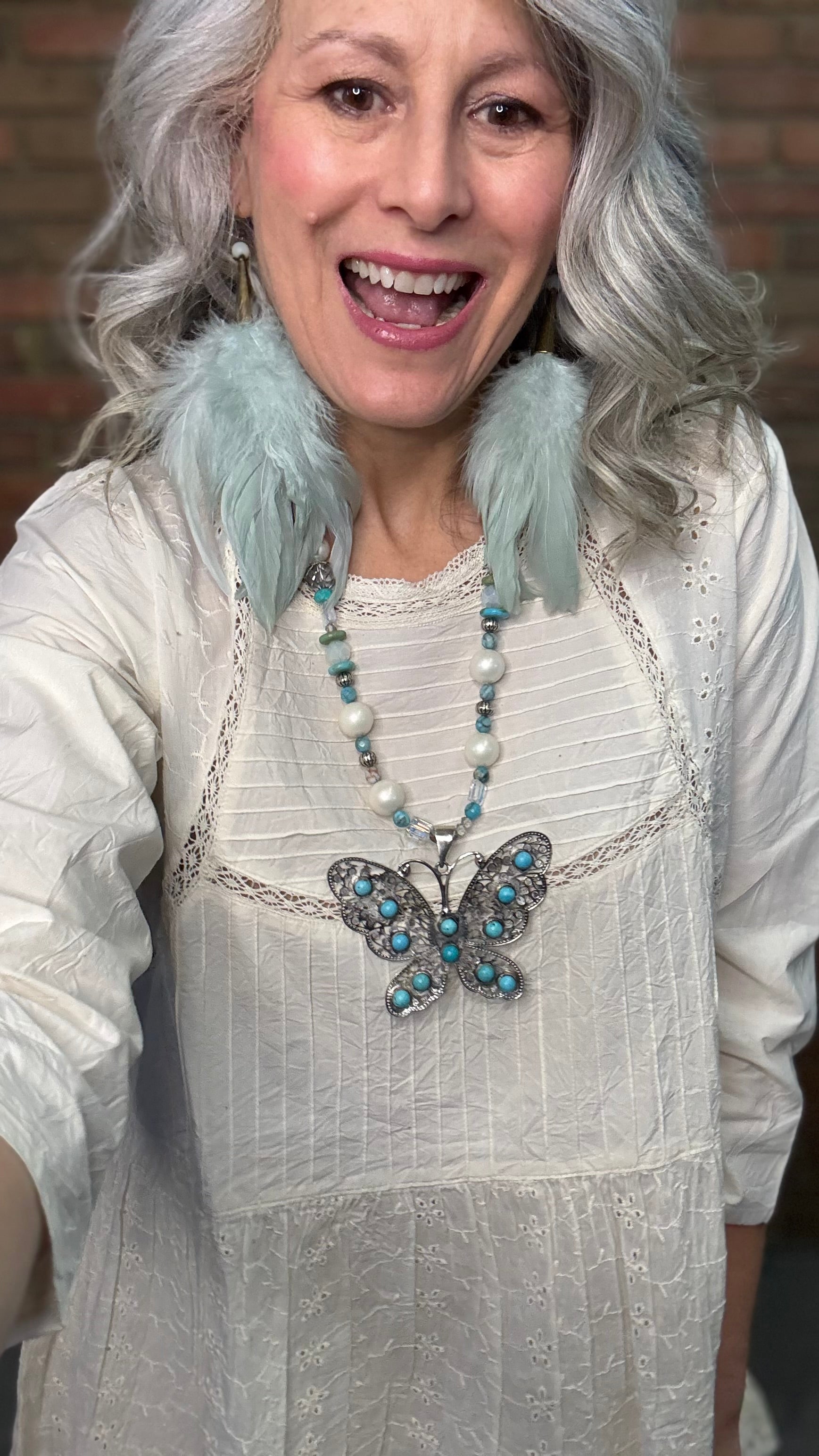 Woman wearing Silver Filigree Butterfly Necklace with turquoise stones and sage feather earrings.