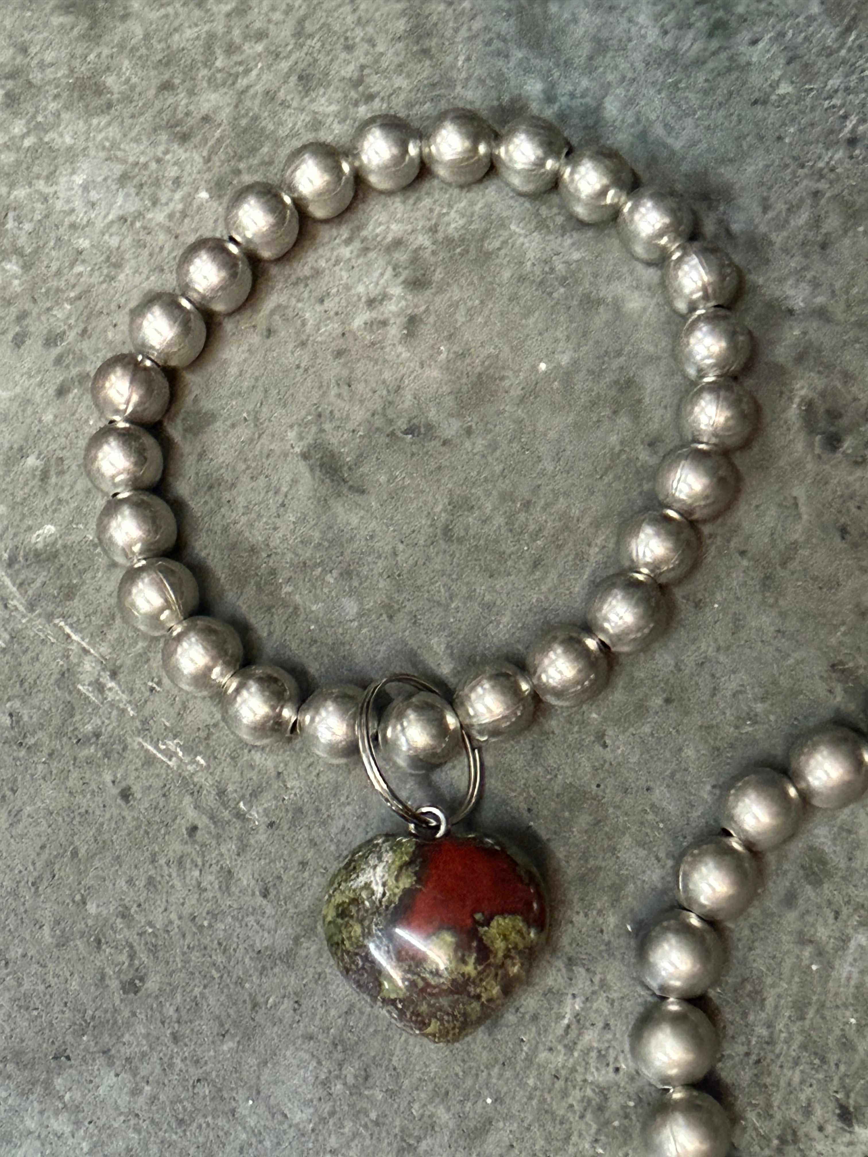 Silver beaded bracelet with a red stone charm on a gray surface