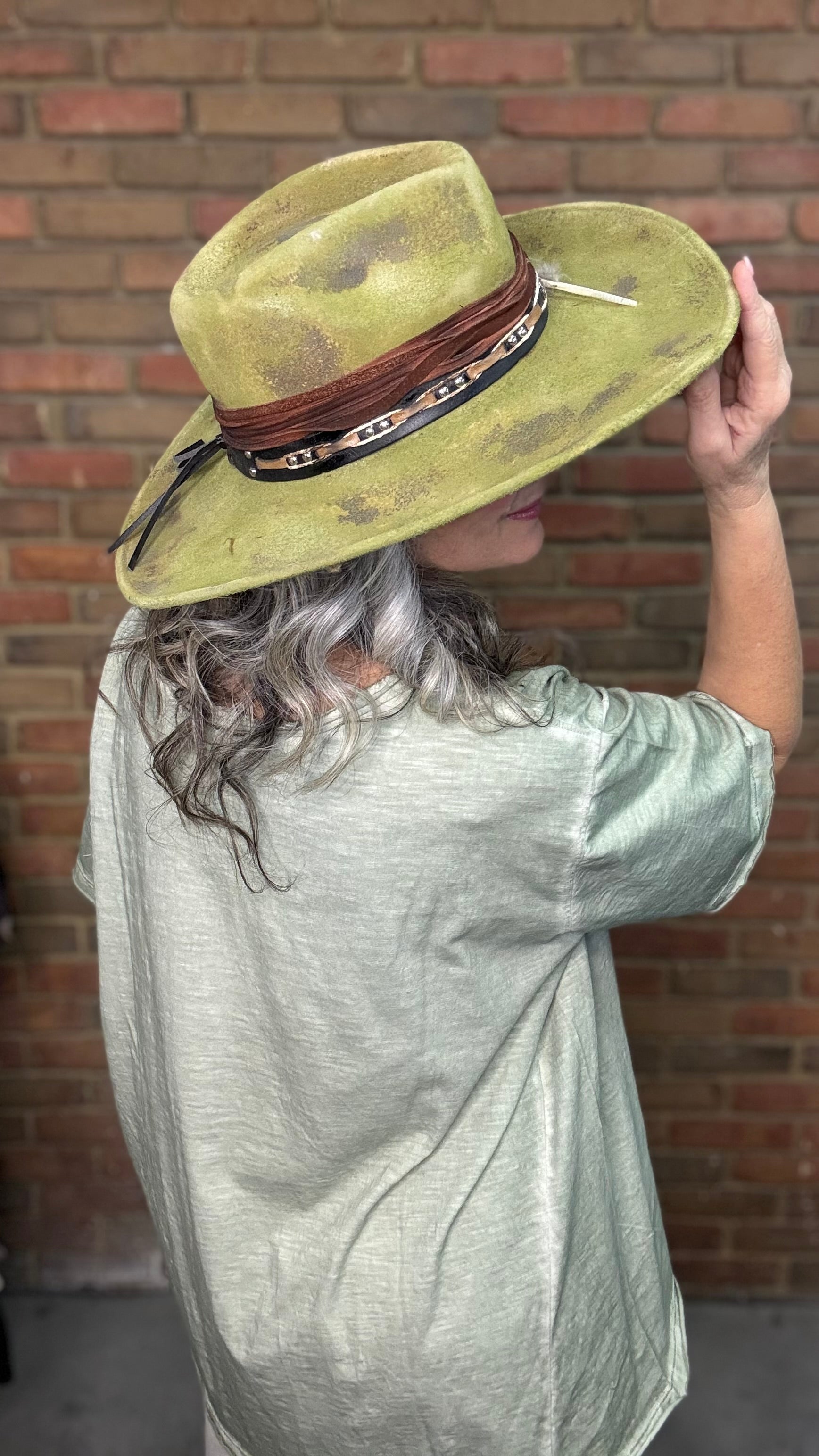 Woman wearing Spirit Feather Hat against a brick wall.