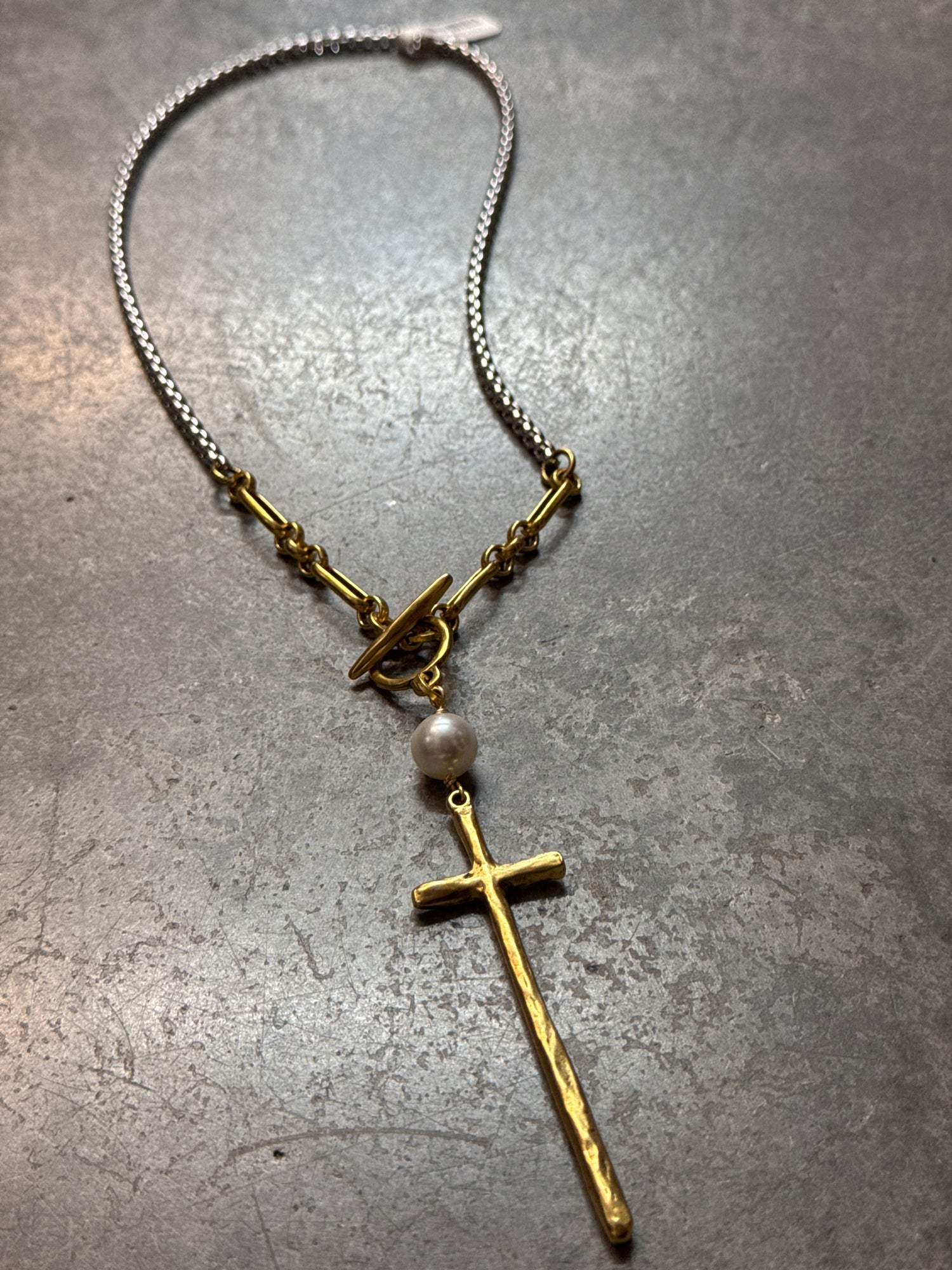 Gold cross necklace with a chain on a gray surface