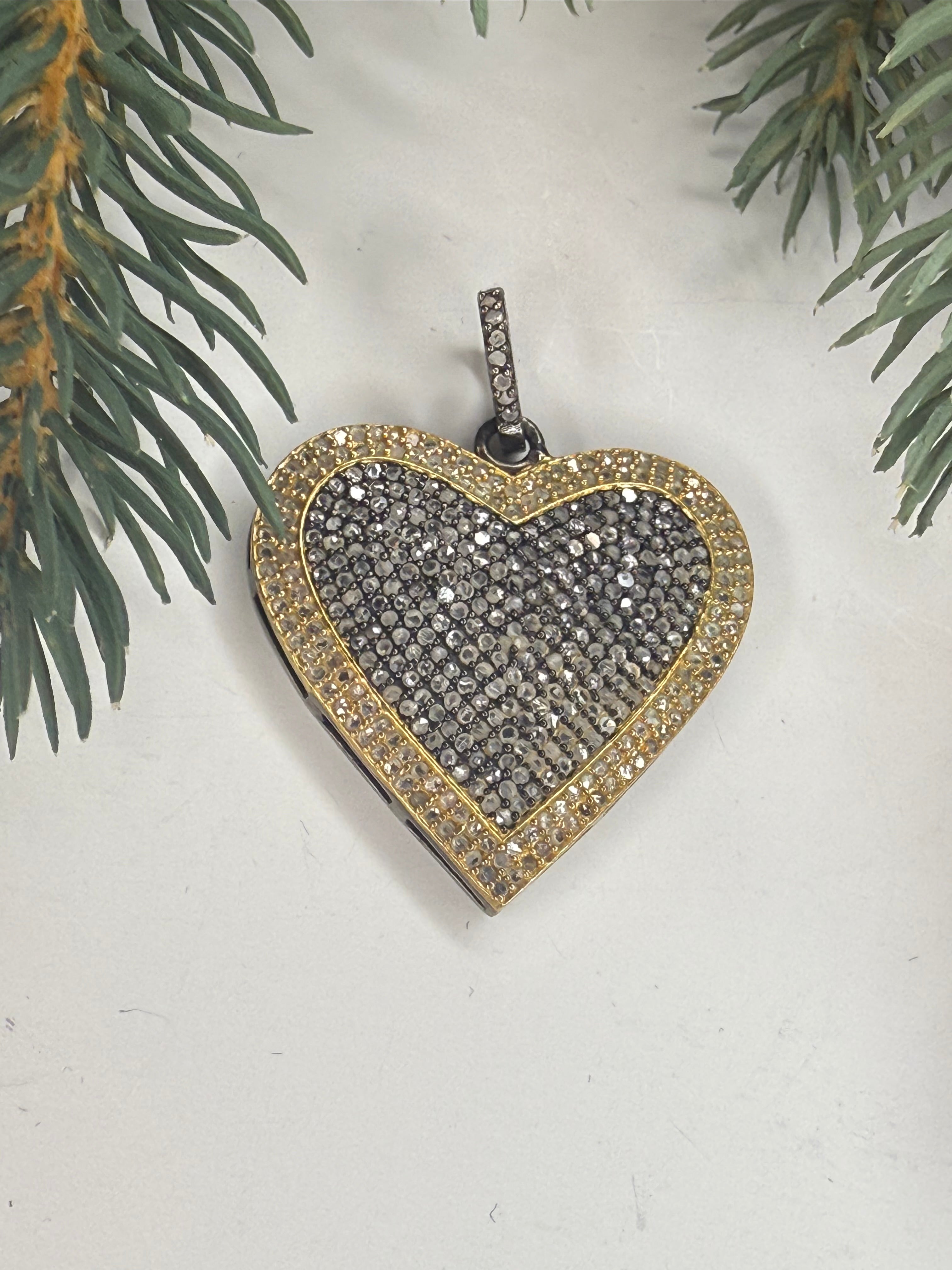 Heart-shaped pendant with gold border and black center all filled with pave diamonds on a light background with greenery.