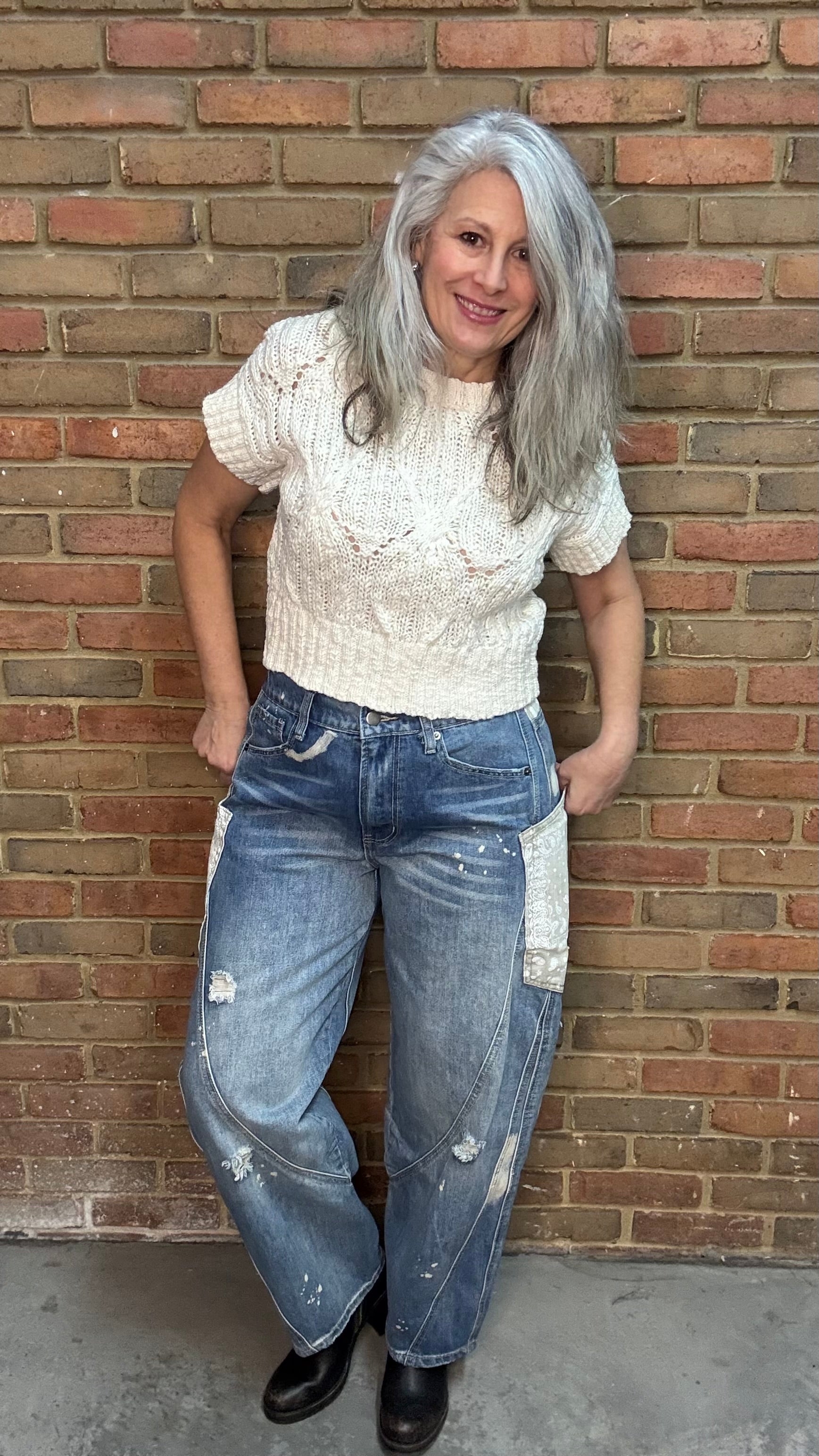 Woman standing in front of a brick wall wearing the Big Pocket Denim Pants and the Oatmeal Sweater Top.