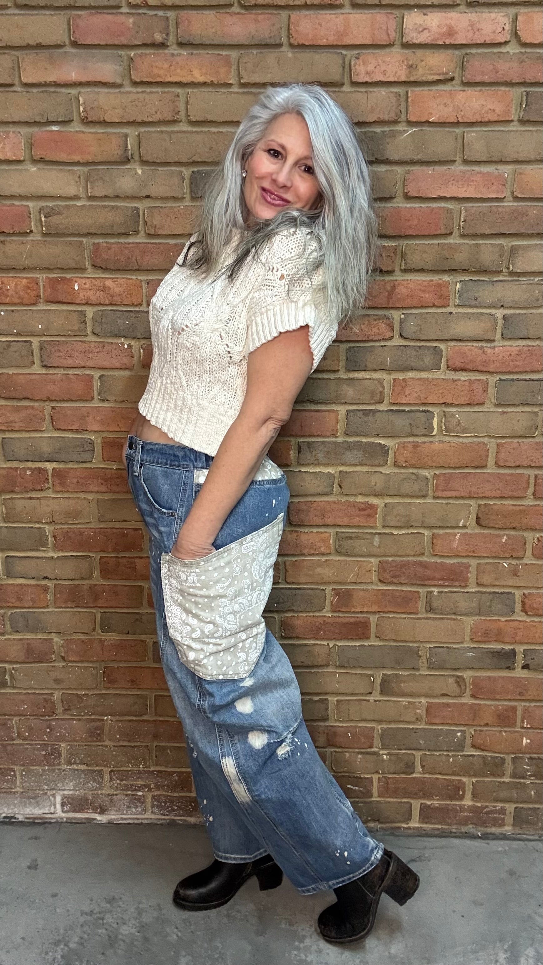 Woman standing in front of a brick wall wearing the Big Pocket Denim Pants and the Oatmeal Sweater Top.