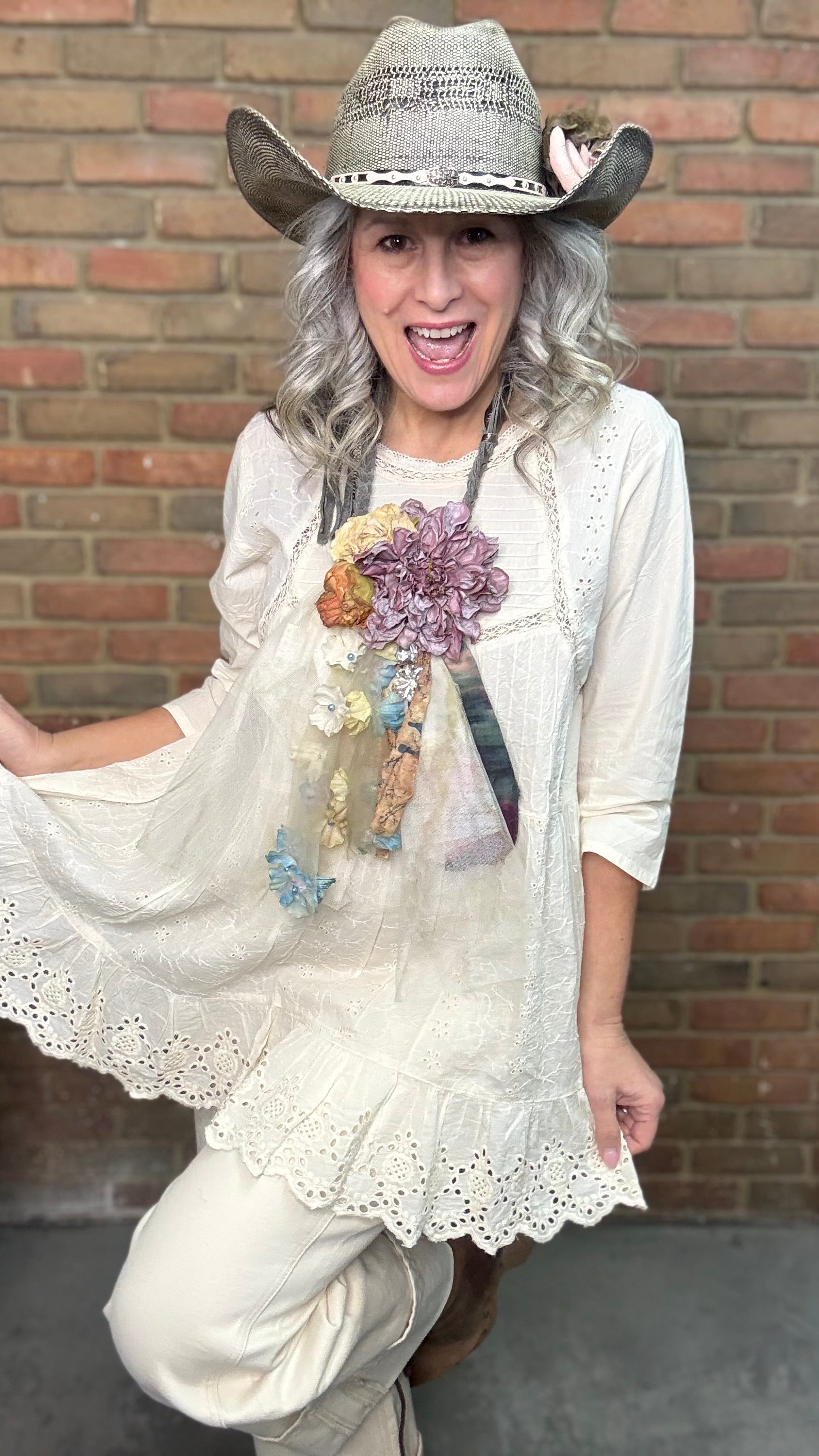 Person wearing a white outfit with Flower Garden Necklace and a cowboy hat against a brick wall.
