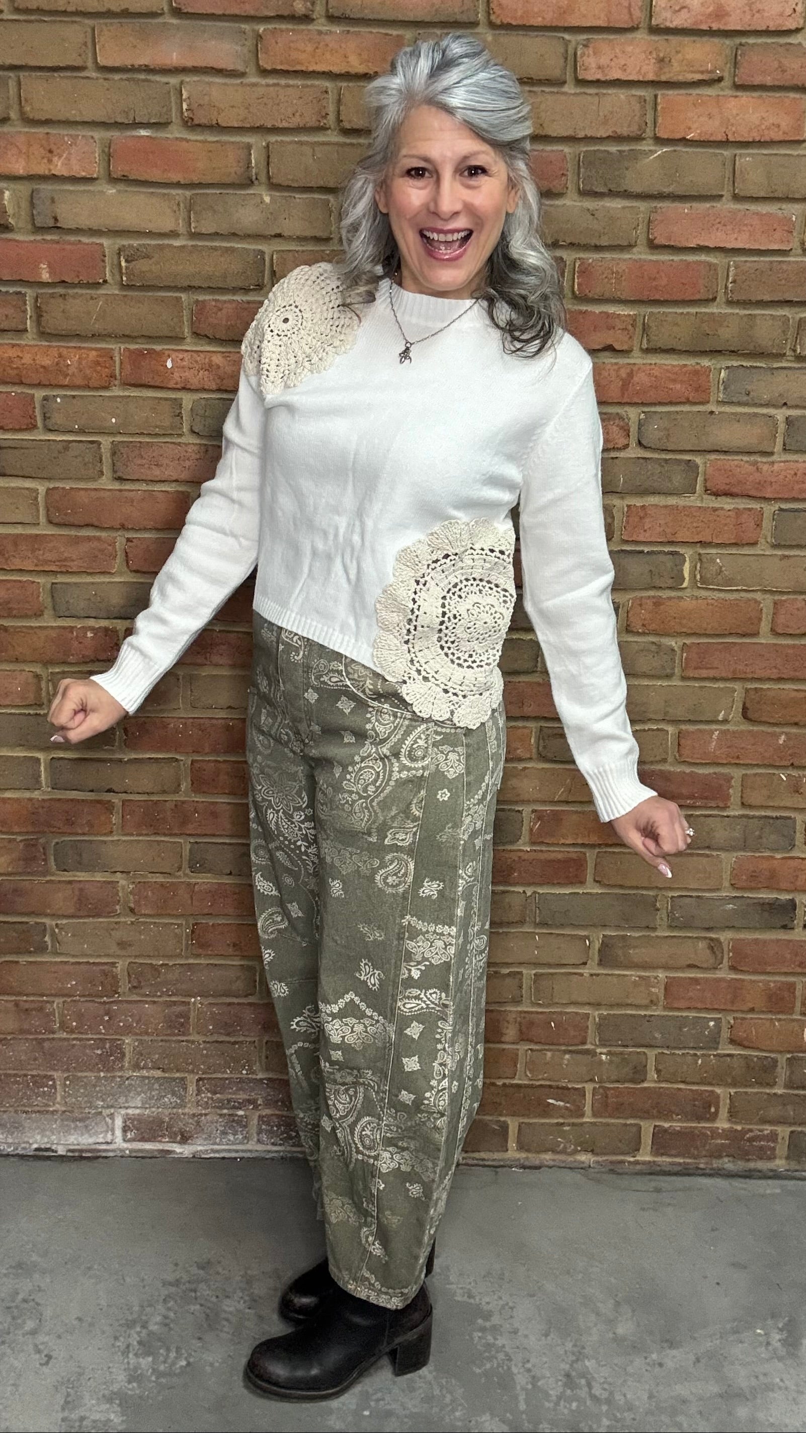 Woman wearing the Crochet Detail Cropped Sweater and the Paisley Print Jean standing against a brick wall.