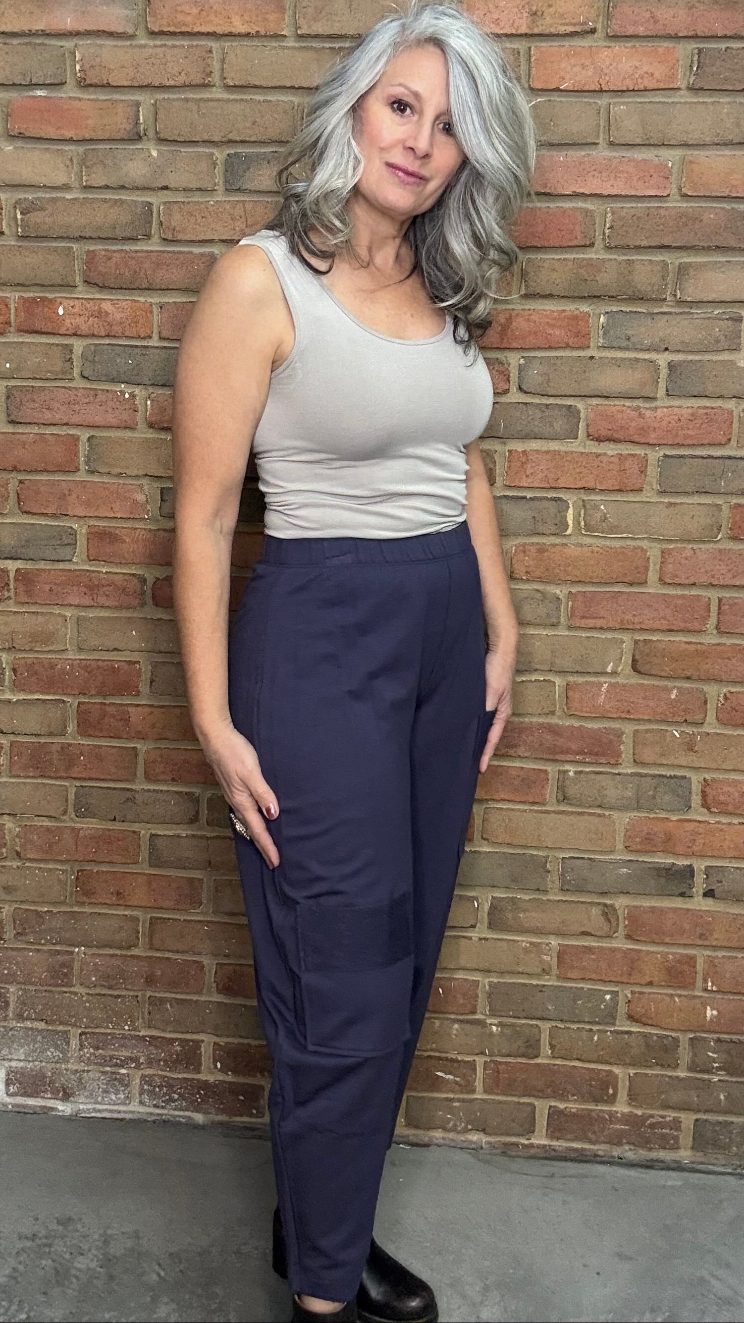 Woman standing against a brick wall wearing a tank top and the Mady Pant in plum.