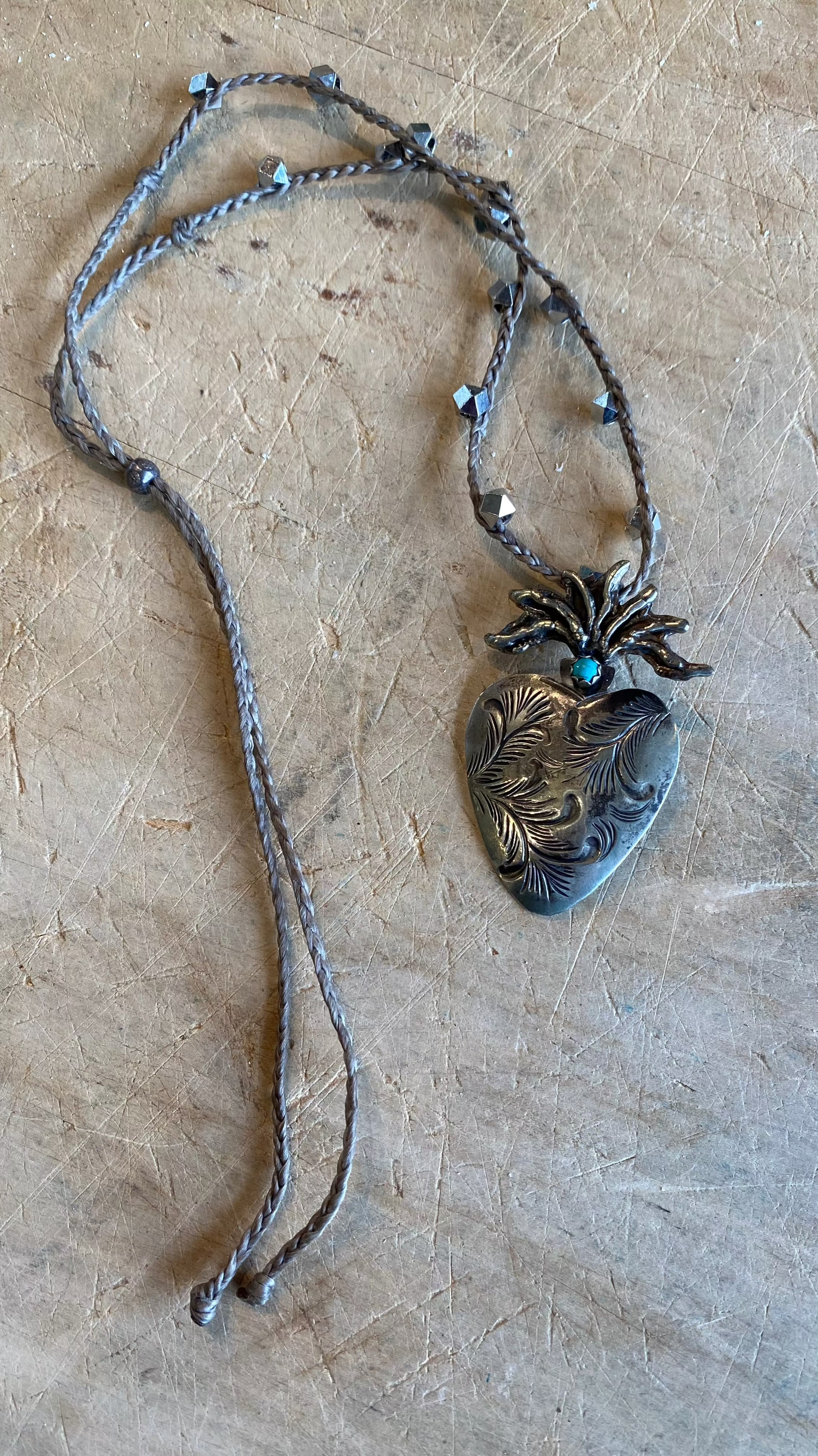 Carved Silver Heart with Turquoise Necklace against a light wooden background