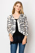 A woman wearing a short cut jacket with a geometric print, featuring a v-neckline and 7/8 length sleeves. The jacket is buttoned up front and she is wearing it over a black top with jeans.