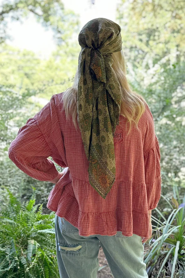 Person wearing a pink top and green scarf with a forest background