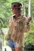 Woman in a floral shirt and denim shorts with a hat, standing in a tropical setting.