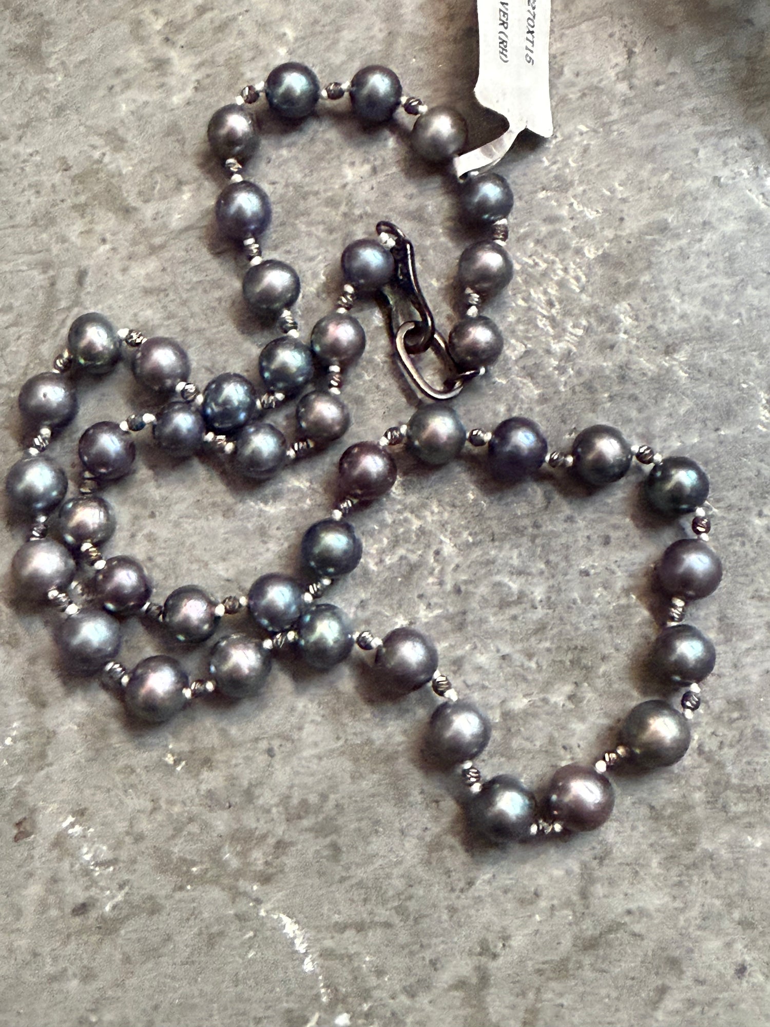 Gray pearl necklace on a textured surface with a visible tag.