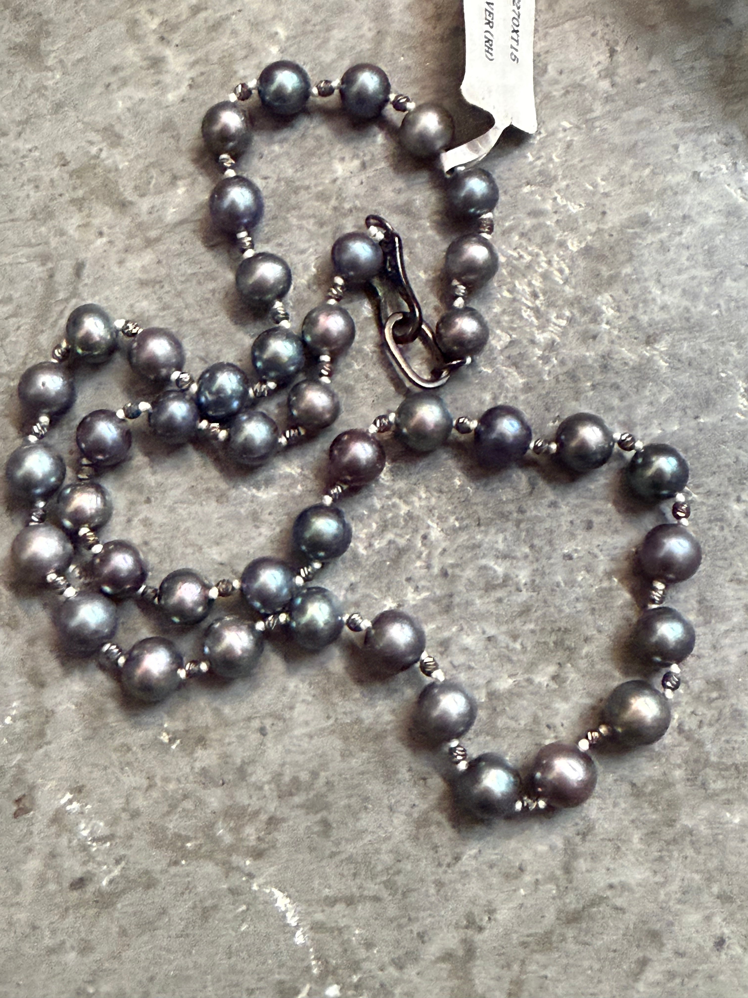 Gray pearl necklace on a textured surface with a visible tag.