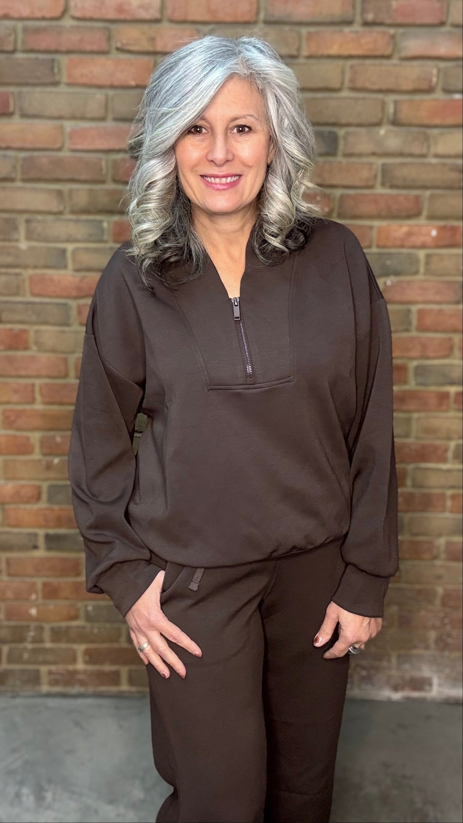 Person wearing a brown outfit standing against a brick wall