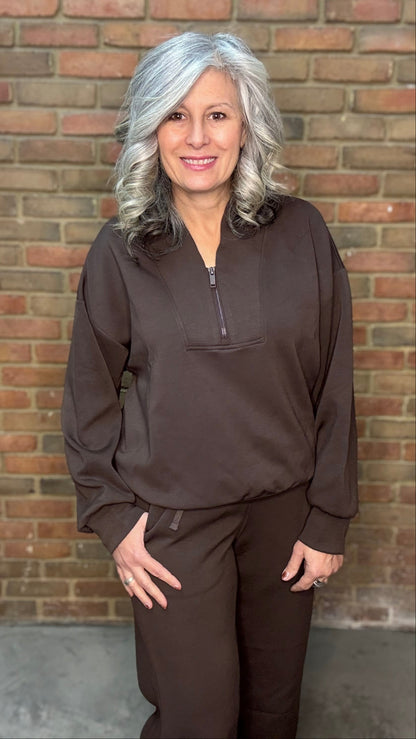 Person wearing a brown outfit standing against a brick wall
