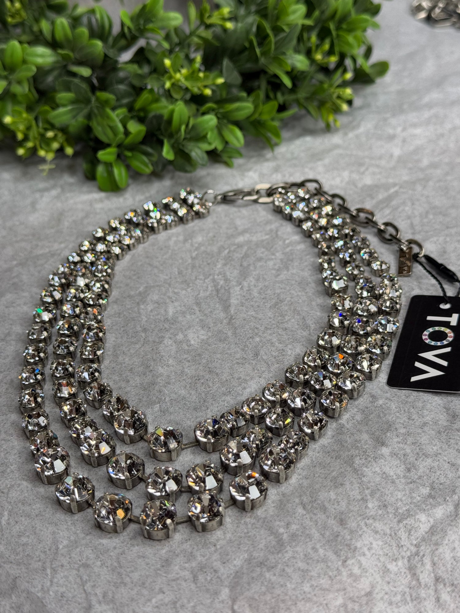 Silver necklace with crystals on a gray surface with greenery