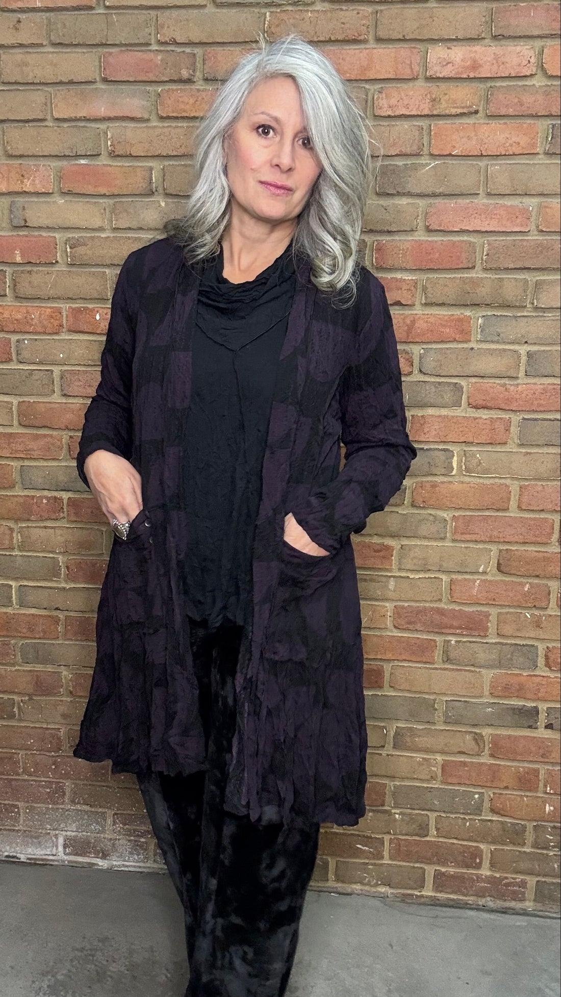 Woman wearing a black outfit standing against a brick wall.