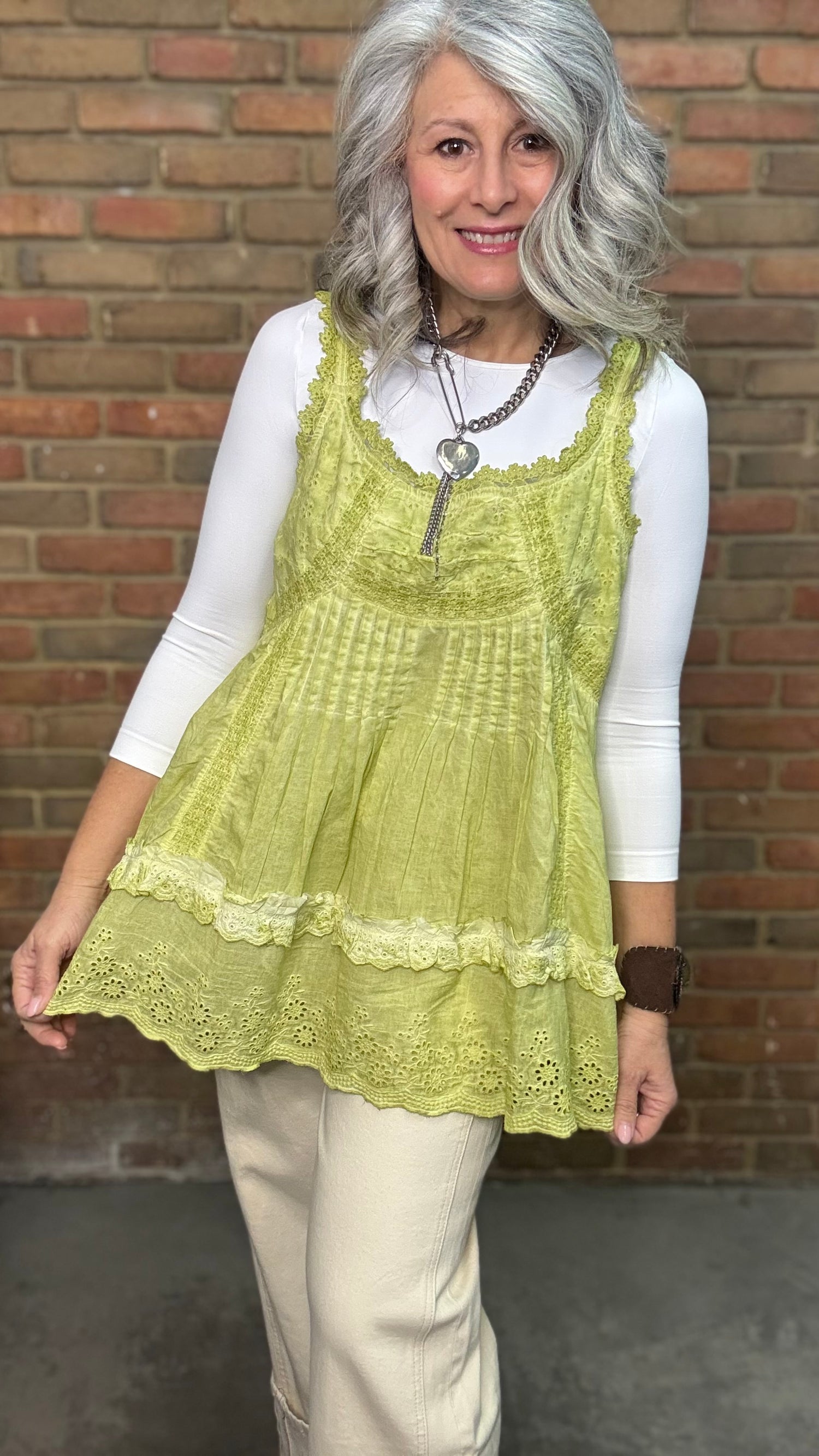 Woman wearing Eyelet Lace Tank over a white shirt, standing against a brick wall.
