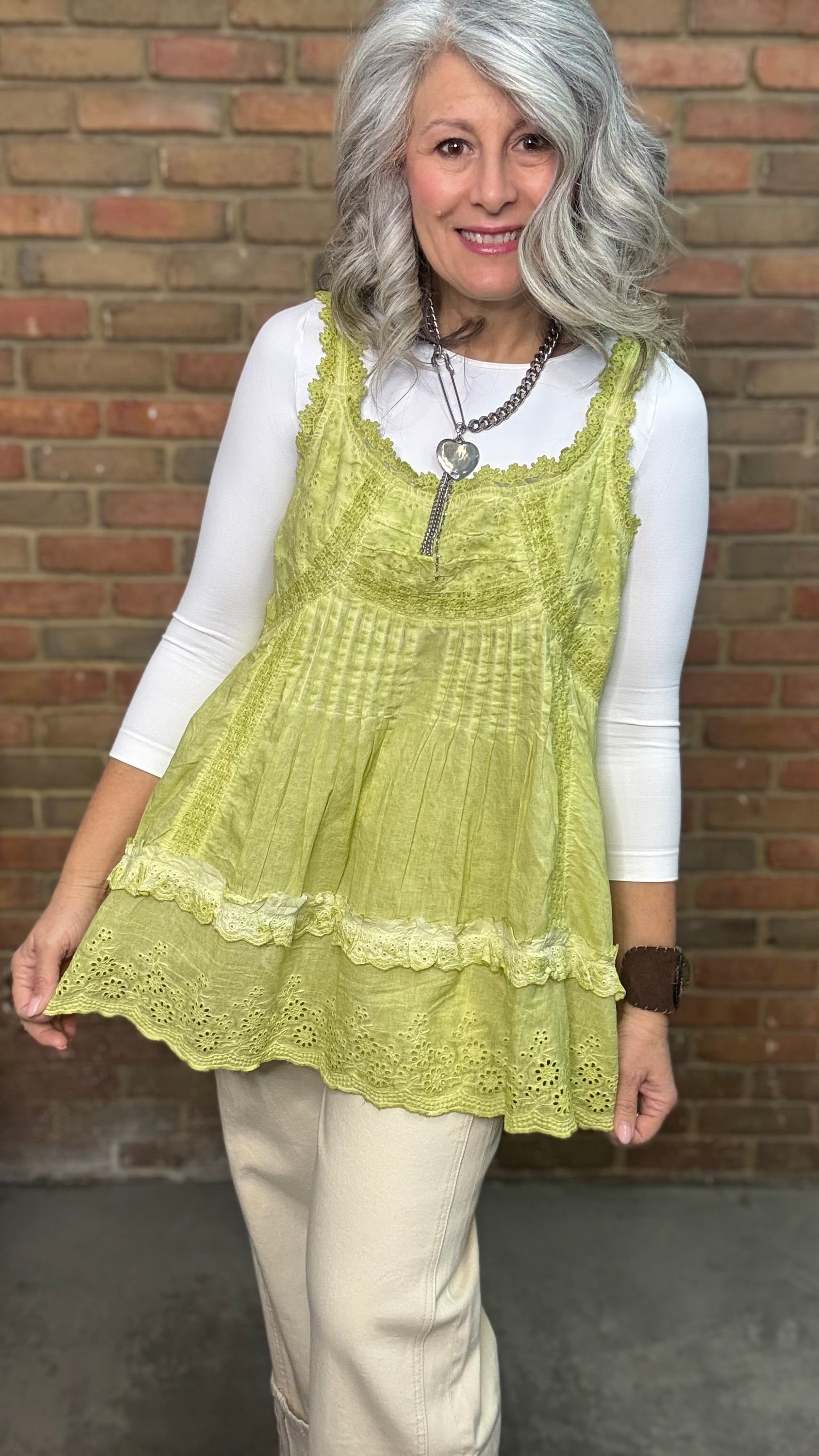 Woman wearing Eyelet Lace Tank over a white shirt, standing against a brick wall.