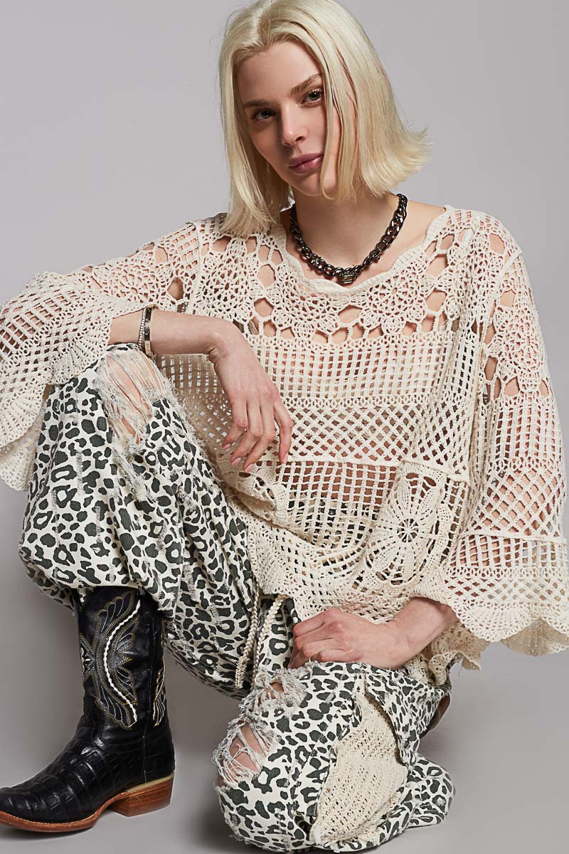 Woman wearing a crochet top and leopard print pants with cowboy boots on a gray background