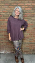 Person wearing a purple sweater and patterned pants standing against a brick wall.