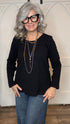 Woman wearing The Black Wanda Round Neck Top layered with the Silver Snake and Gold Paperclip Chain Necklace, the Silver Snake and Gold Paperclip Chain Choker Necklace and the Gold Cross w/Pearl Necklace  paired with  Judy Blue Palazzo jeans indoors against a white paneled wall.