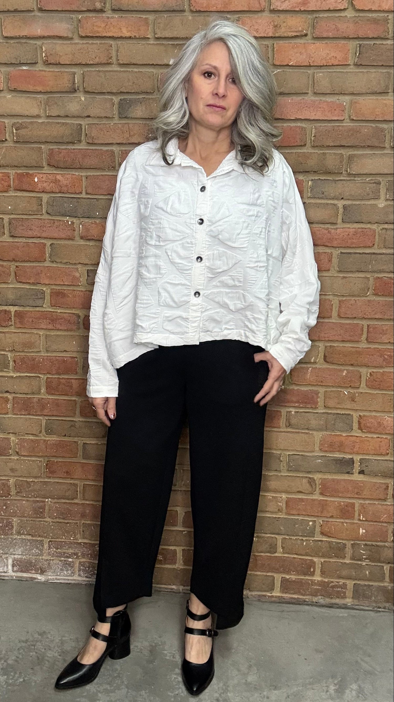 Person wearing a white shirt and black pants against a brick wall