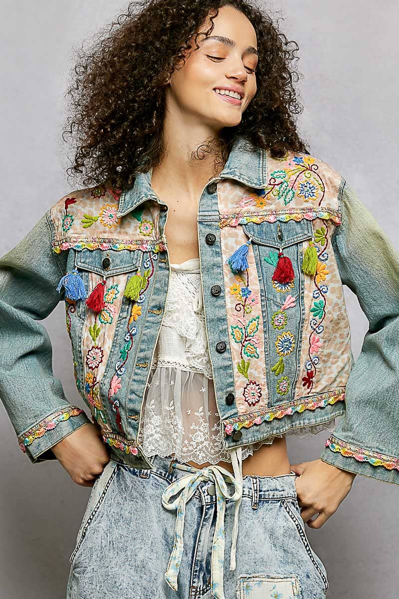 Woman wearing a colorful embroidered denim jacket against a gray background