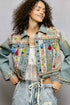 Woman wearing a colorful embroidered denim jacket against a gray background