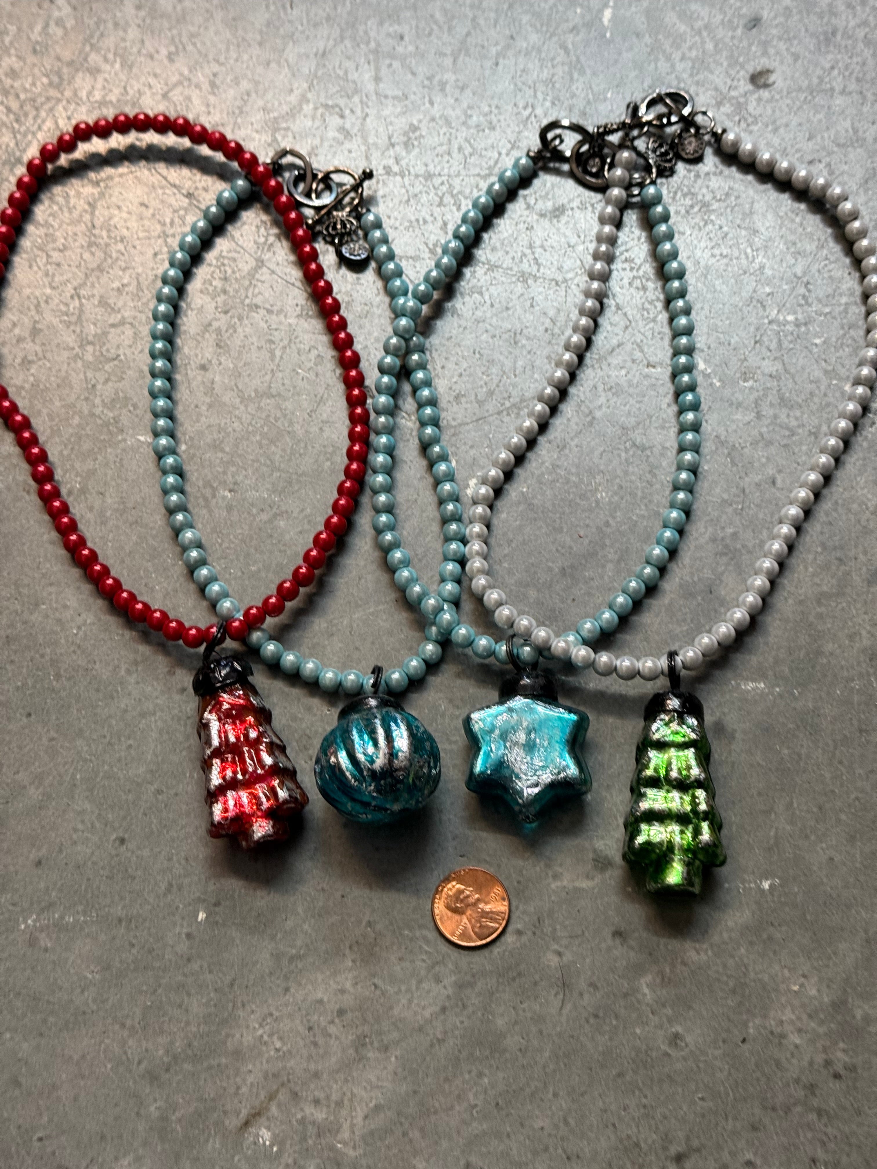 Four beaded necklaces with colorful beads on a gray surface, one next to a penny for scale.