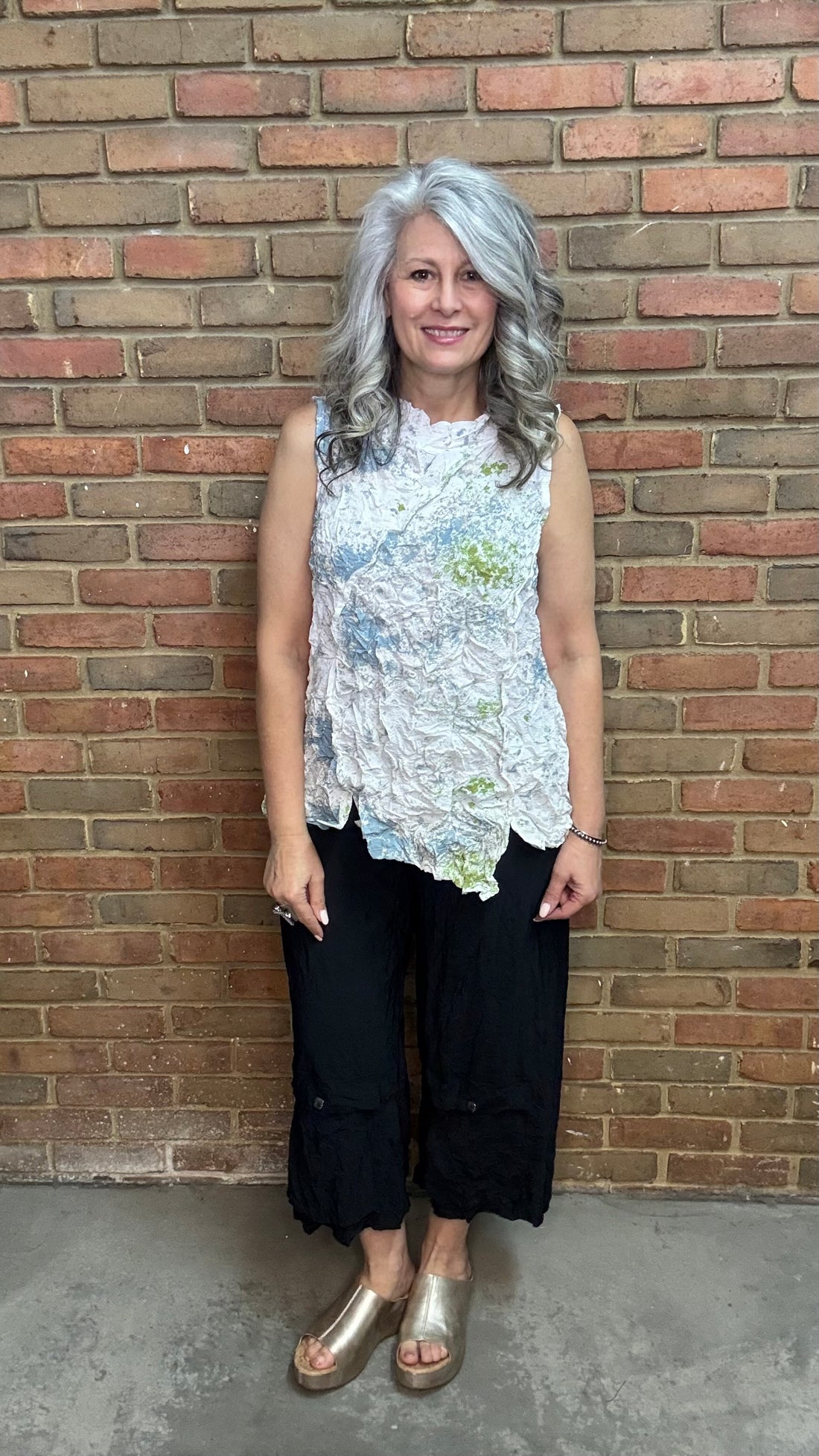 Woman standing against a brick wall wearing Levana Tank - Fiji and black pants.
