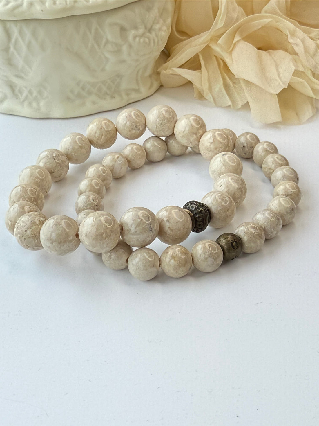 Beige stone beads on a white surface with a textured beige object and fabric.