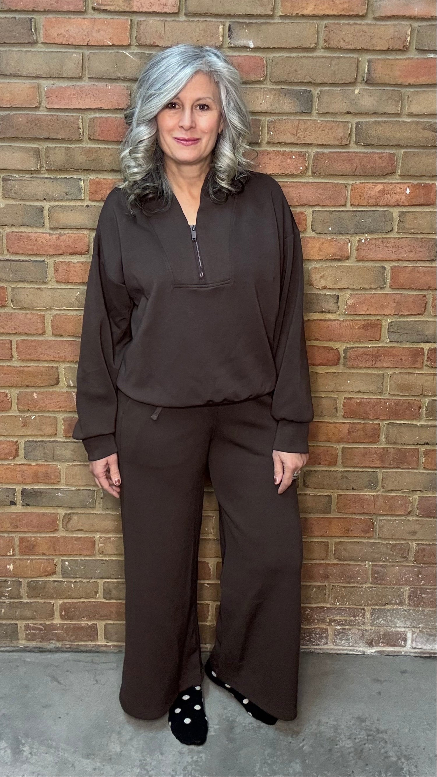Woman in brown outfit standing against a brick wall