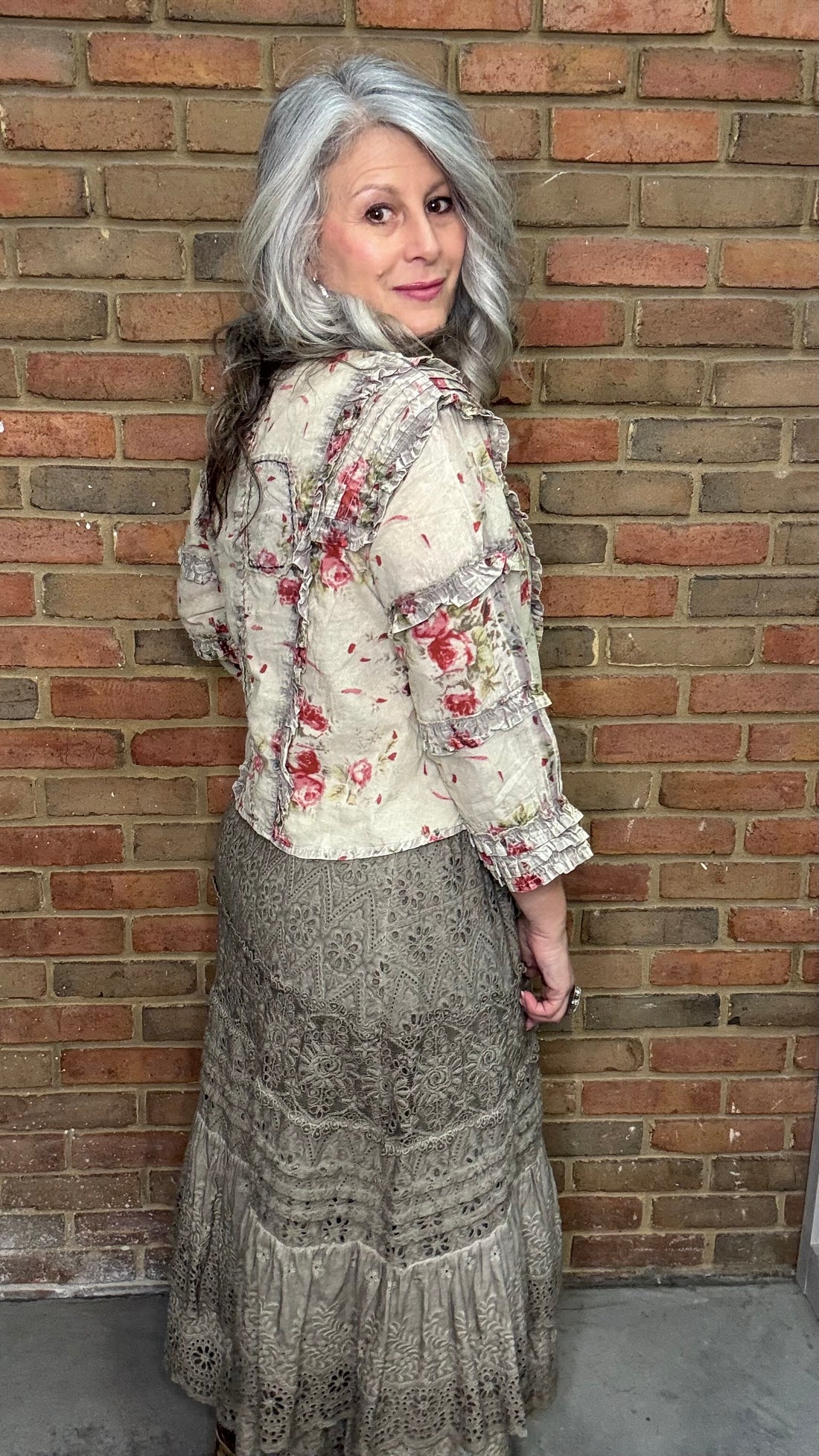 Woman wearing a Vintage Wash Pin Tuck Ruffle Trim Top standing against a brick wall.