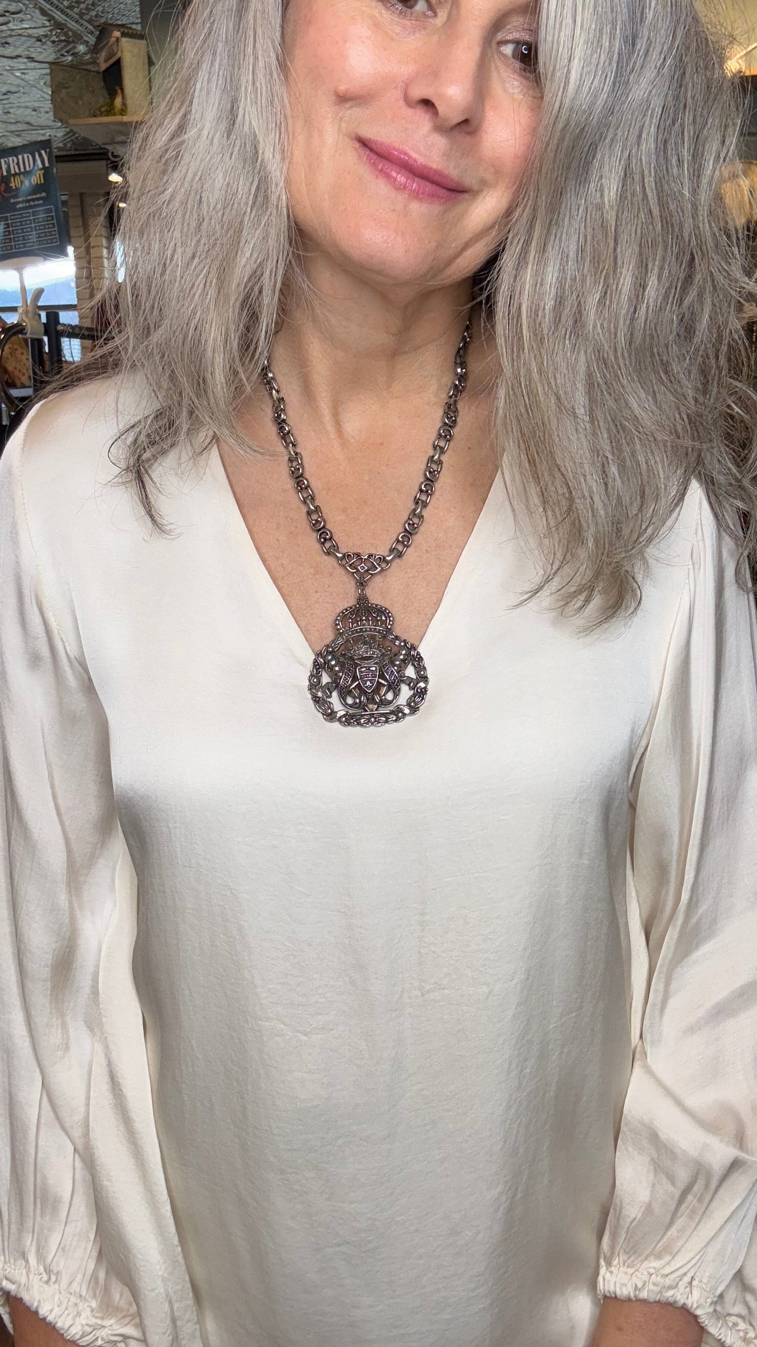 Woman with gray hair wearing a white top and necklace in an indoor setting