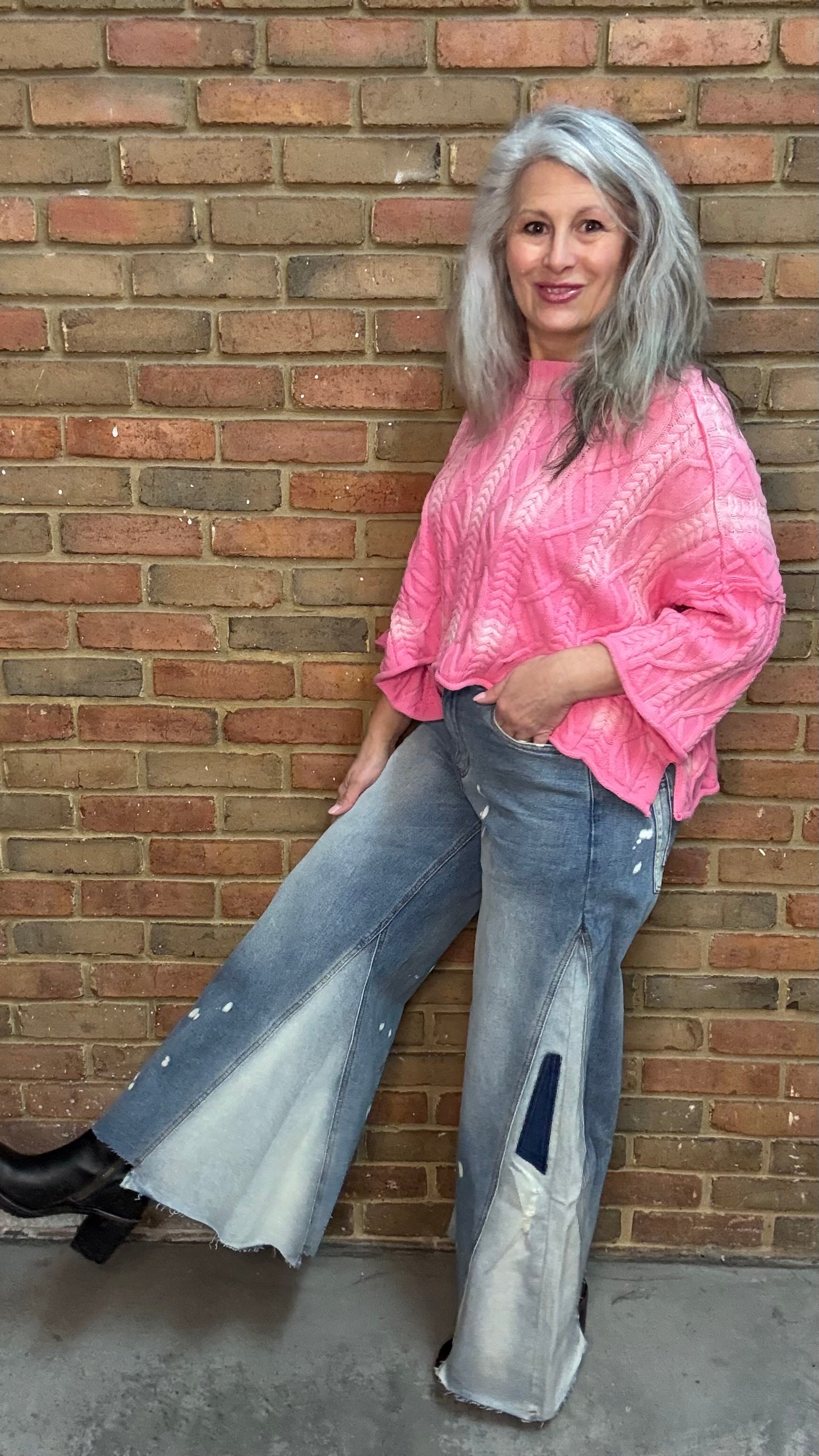 Woman wearing Bleached Wide Leg Jeans and Dusty Pink Ombre Sweater standing against a brick wall.