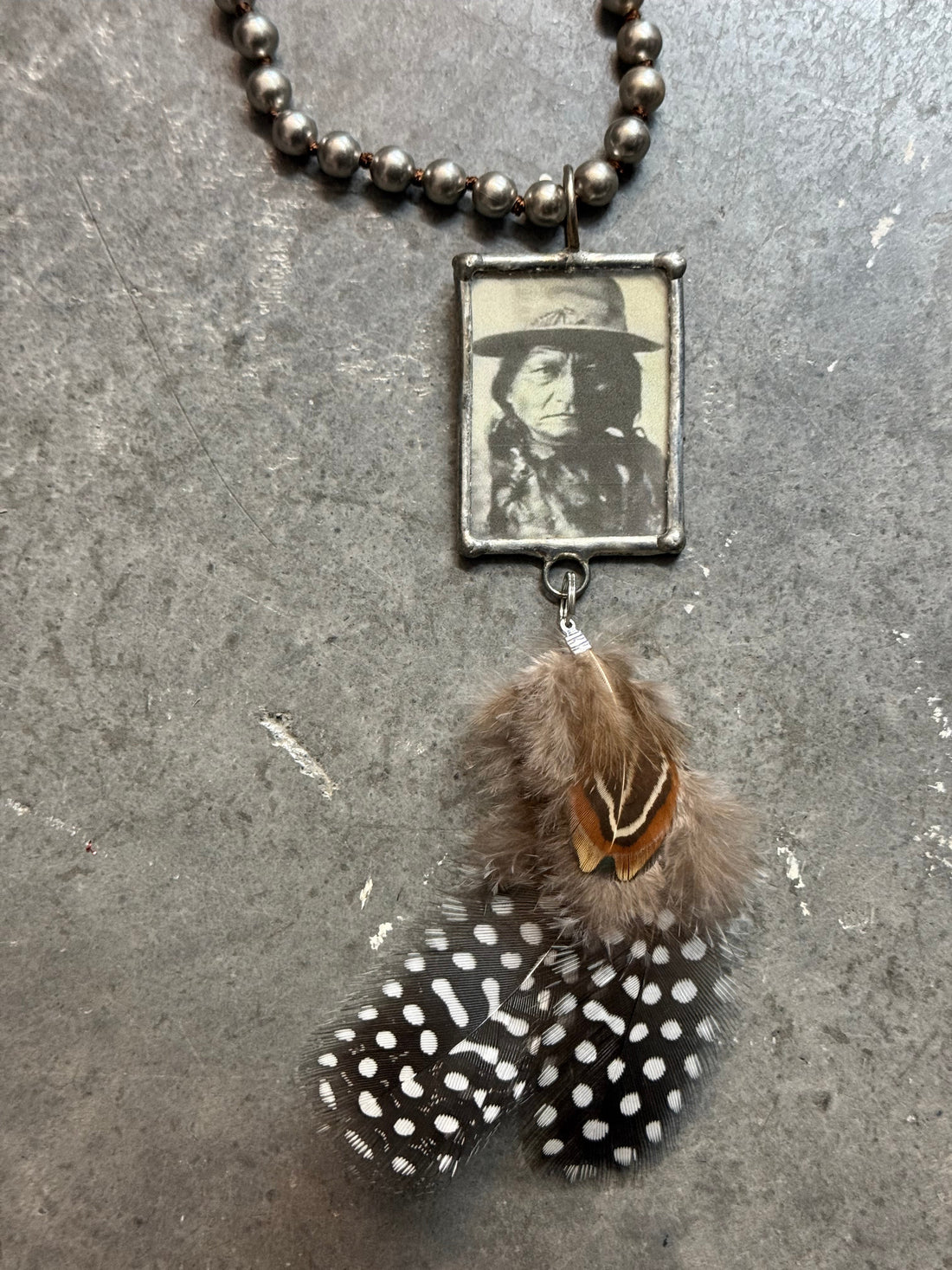 Necklace with feather and vintage-style photo charm on a textured surface